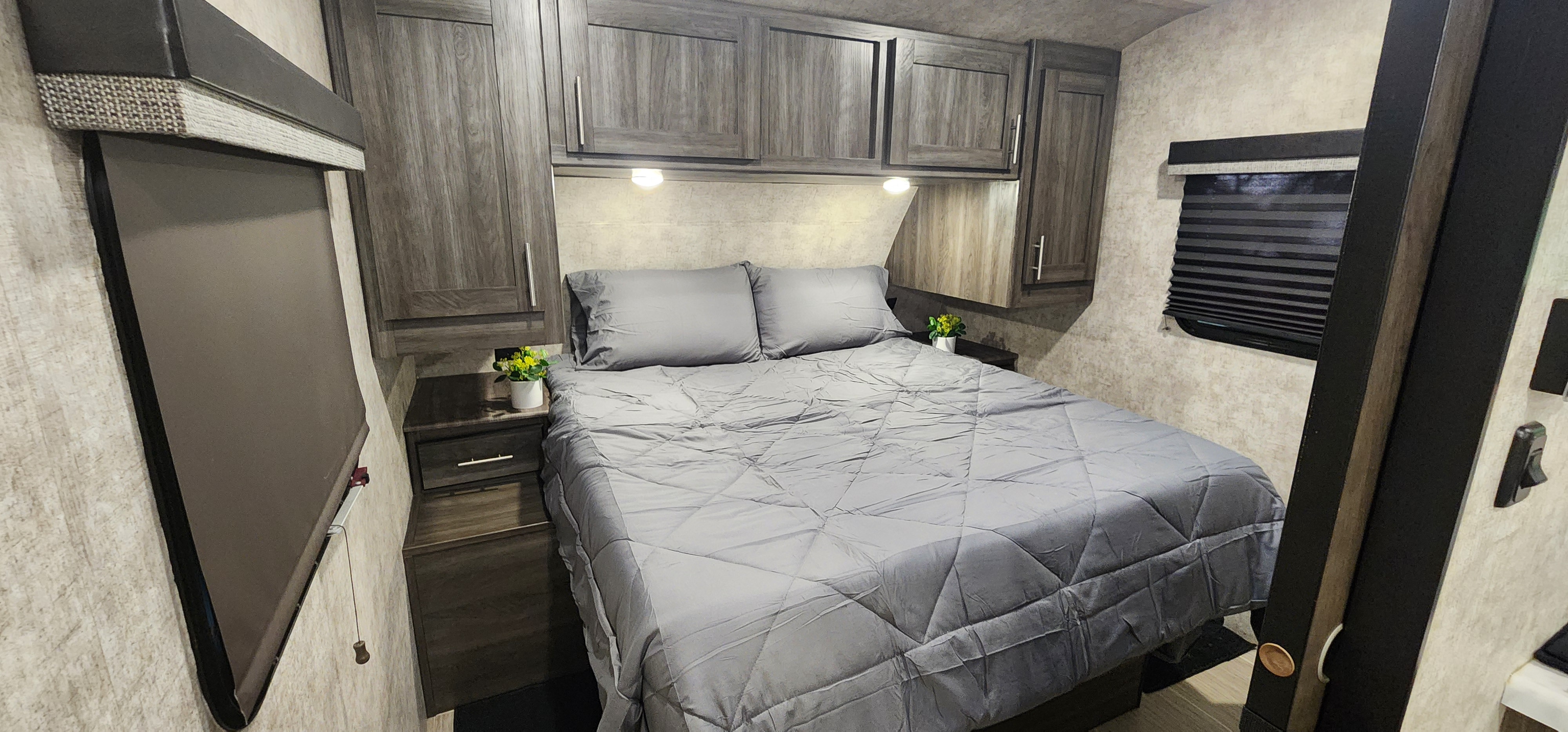 Comfortable RV rental bedroom featuring a gray bed, ample overhead storage, and bedside lighting.. Highland Ridge RV Mesa Ridge Lite 2018