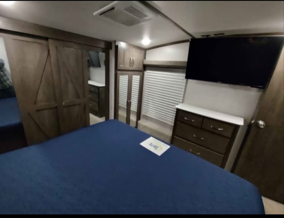Inside an RV rental: a spacious bedroom featuring a blue bed, wall-mounted TV, dresser, and stylish barn-door closets.. Astoria Astoria Trailer 2021