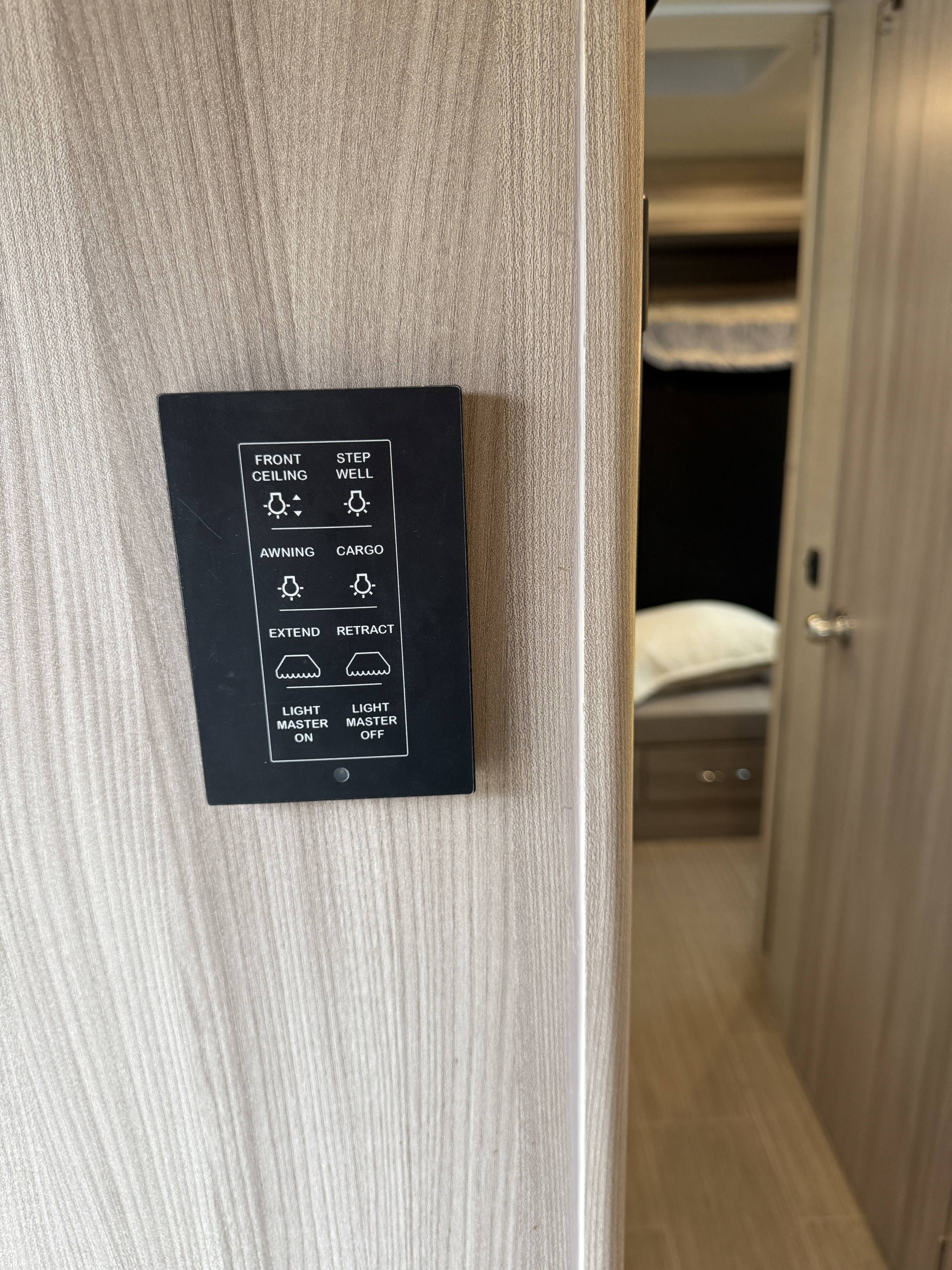 RV rental interior: A control panel on a light wood wall, managing lights (ceiling, step well, awning, cargo) and extend/retract.. Thor Tiburon 2022
