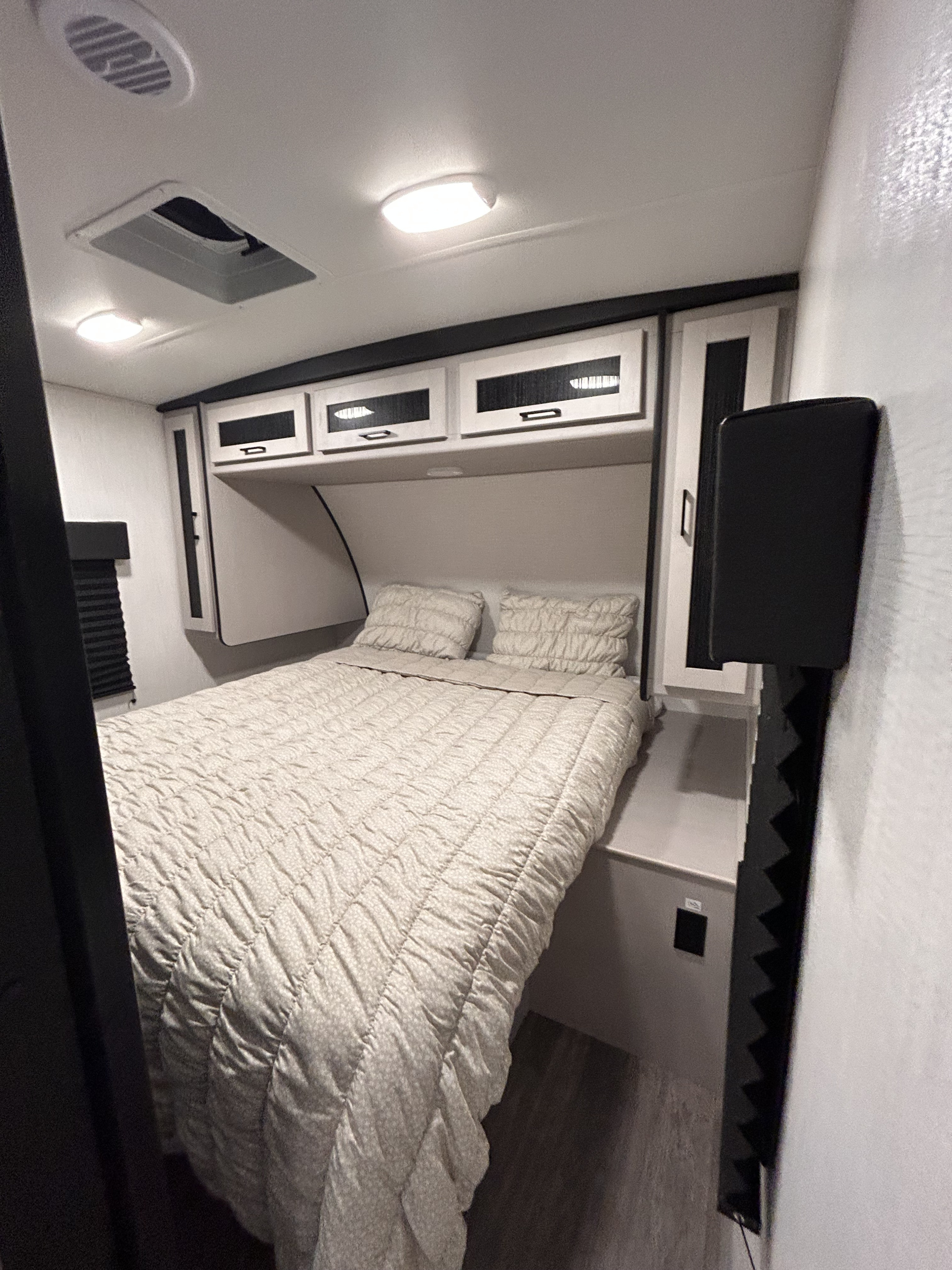 Step into comfort in this RV rental bedroom featuring a full bed, sleek overhead cabinets, and bright lighting.. Heartland RVs Mallard 2024