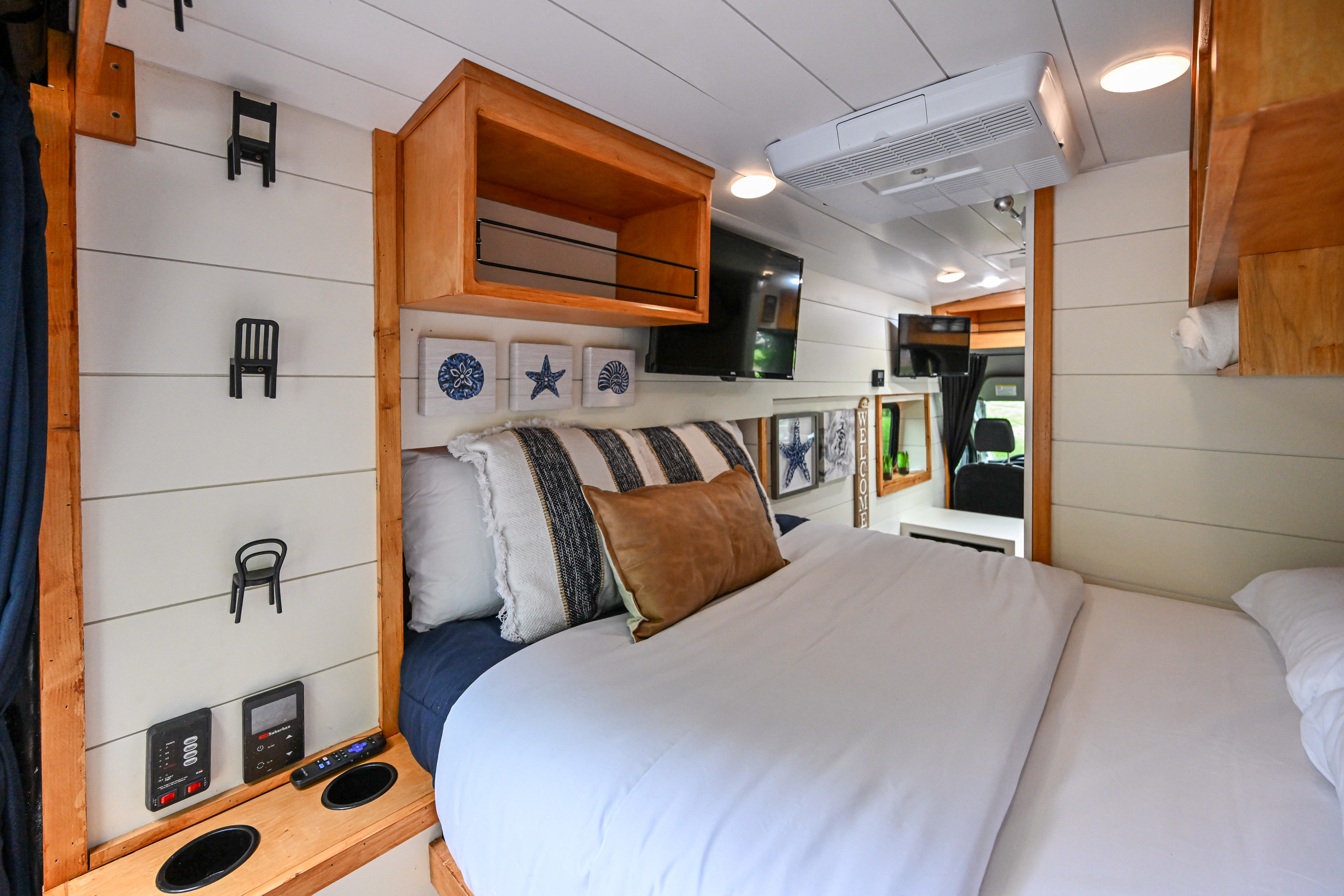 Inside a comfortable RV rental: a modern bedroom with a large bed, coastal art, and convenient controls.. Ford Transit 2022