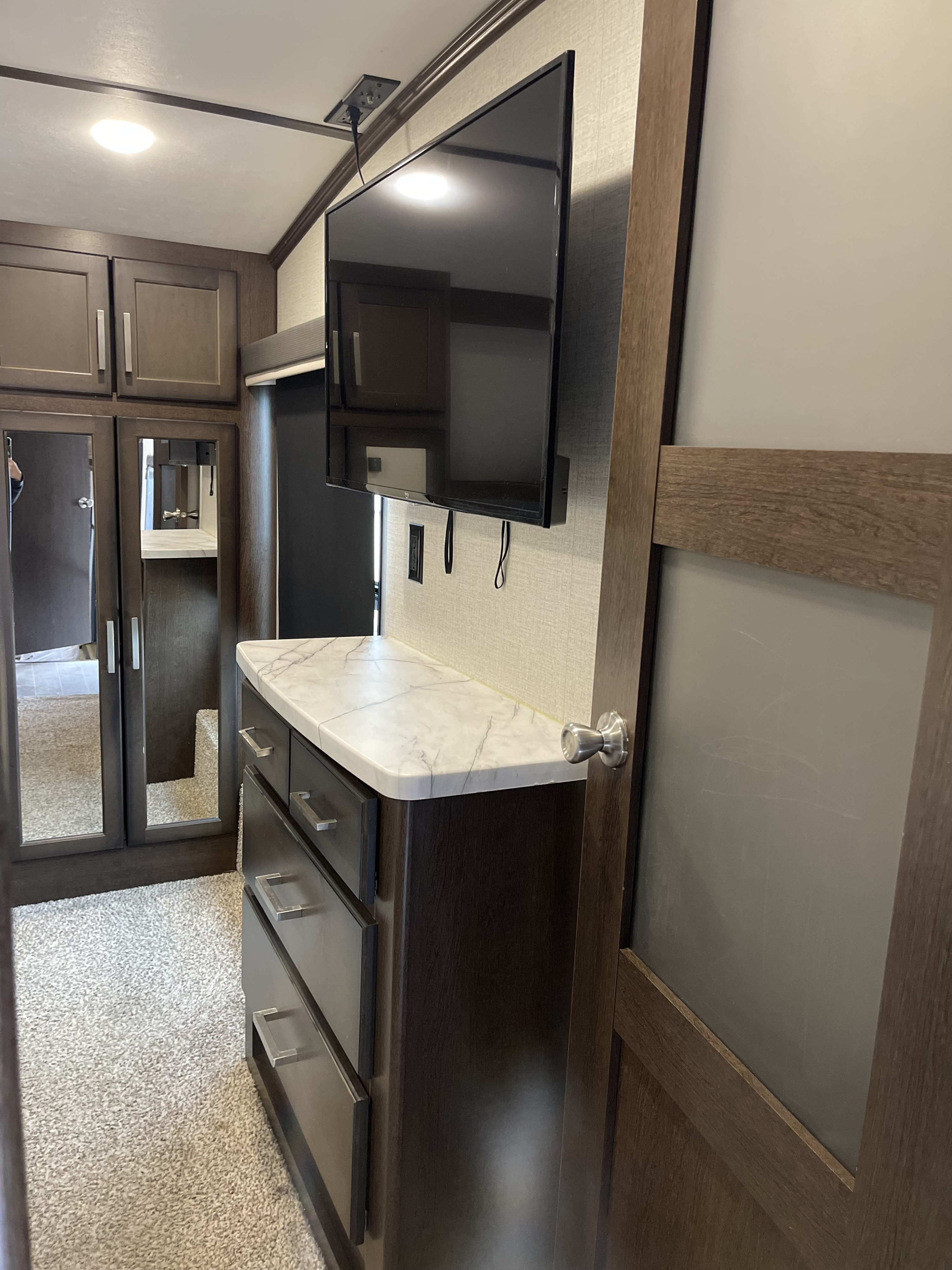 RV rental interior: bedroom area with wall-mounted TV, marble-top dresser, and mirrored closet for storage.. Dutchmen 3602LFKB 2021