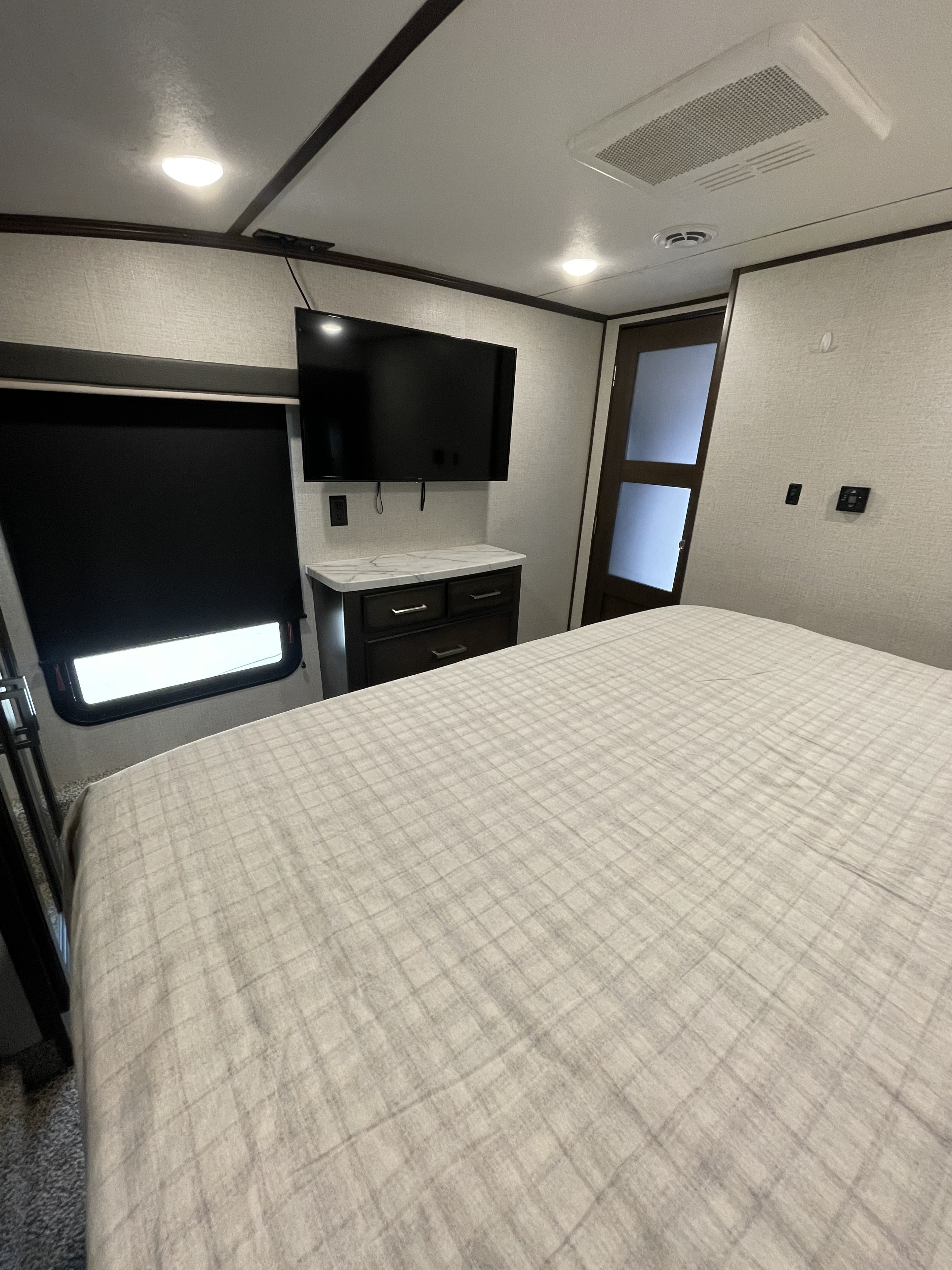 Step inside this cozy RV rental bedroom, featuring a large bed, wall-mounted TV, dresser, and a door for privacy.. Dutchmen 3602LFKB 2021