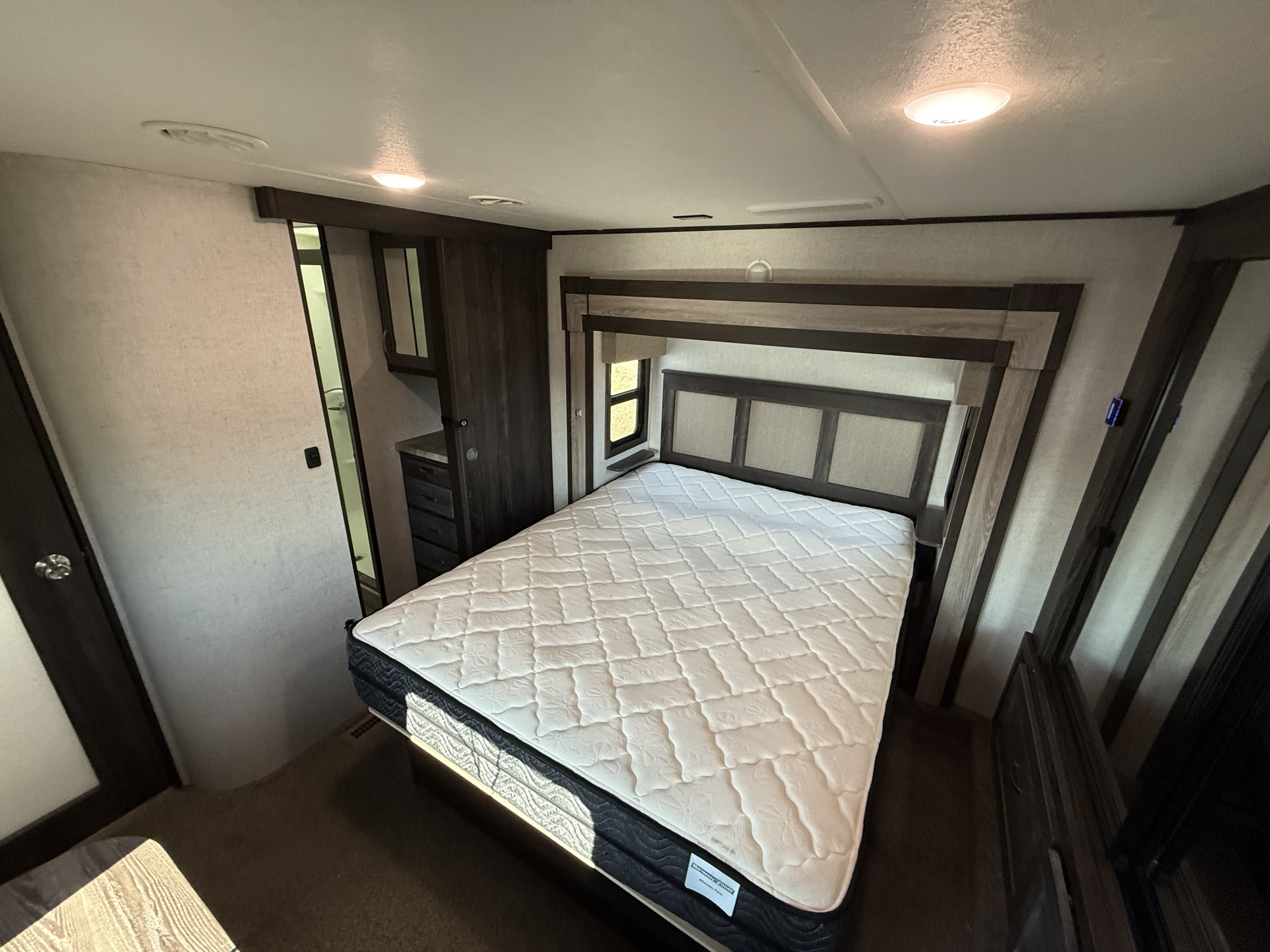 Cozy rv rental bedroom featuring a queen bed with headboard, built-in storage, and bathroom access.. Highland Ridge RV Open Range 2020