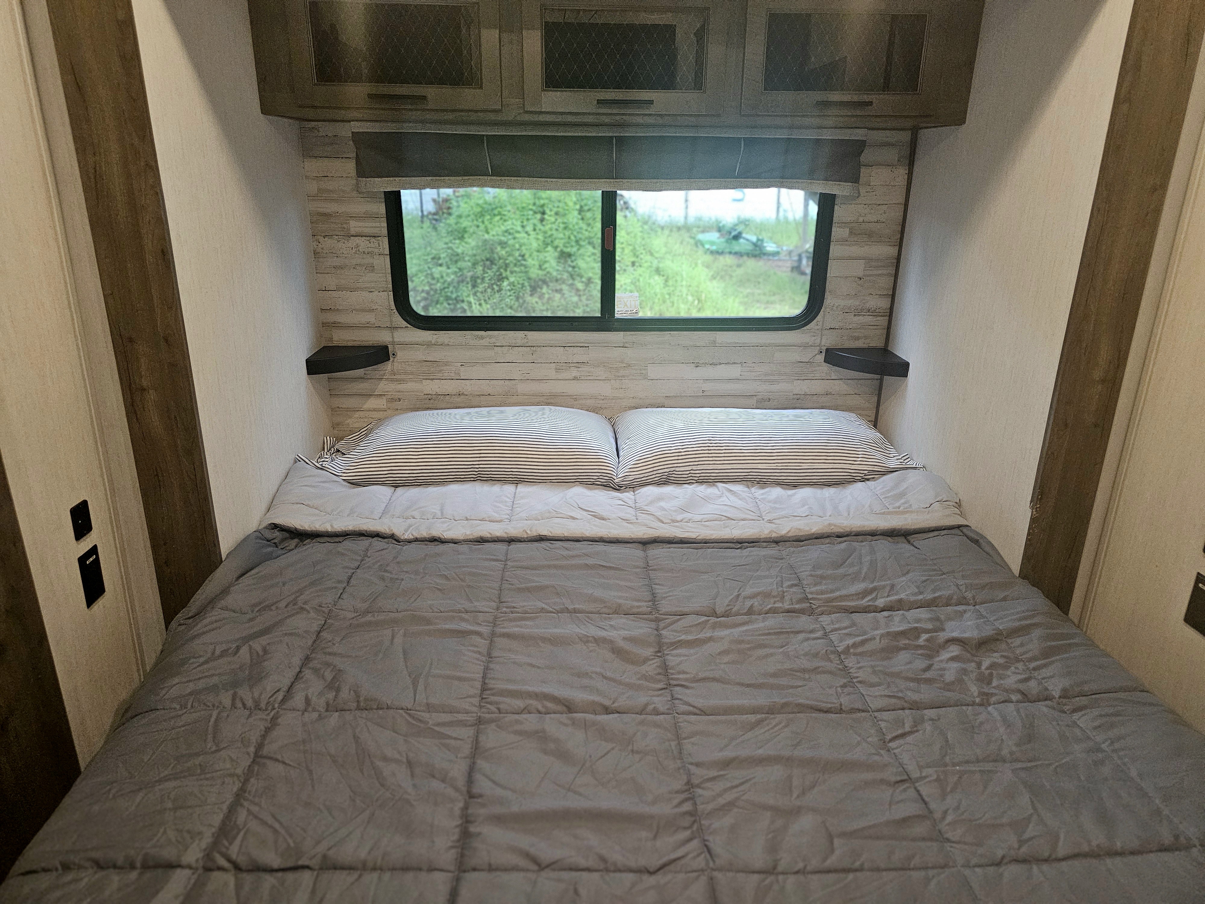 Cozy RV rental bedroom with a comfy bed, striped pillows, and a window view of nature.. Forest River Sabre 2023