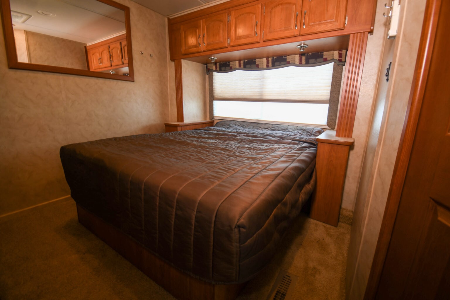 Cozy RV rental bedroom featuring a comfortable bed, wooden overhead cabinets, and a window for your travels.. Monaco Safari 2009