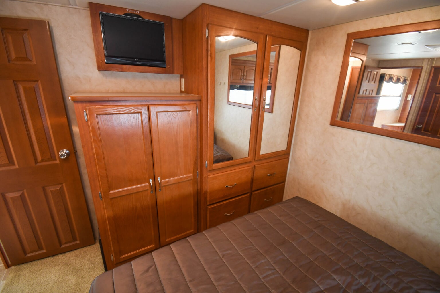 RV rental bedroom with rich wood cabinetry, integrated storage, a mounted TV, comfortable bed, and mirrors.. Monaco Safari 2009