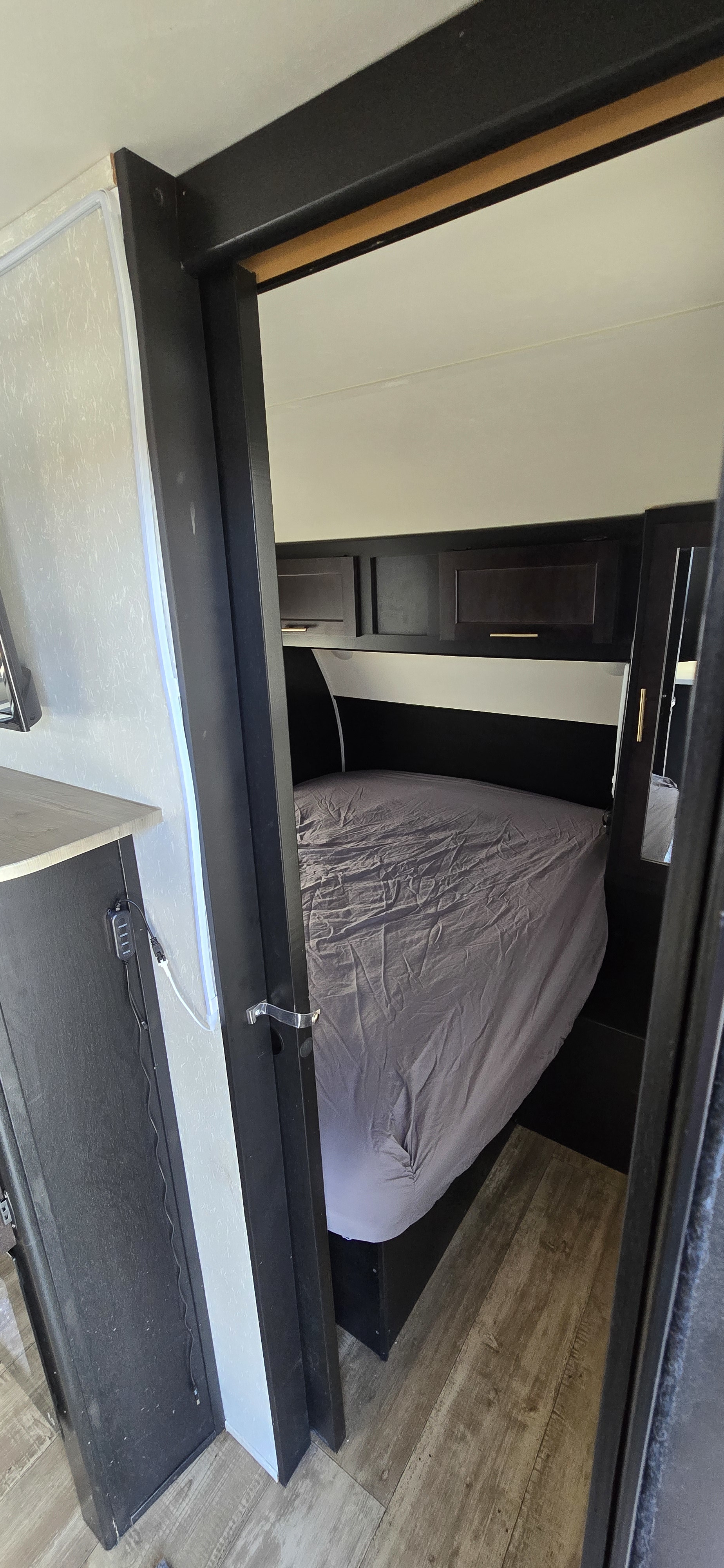 Cozy RV rental bedroom showing a gray bed, dark overhead cabinets, wood-look floor, and a bright LED light strip on the left.. Forest River Cherokee Grey Wolf 2021