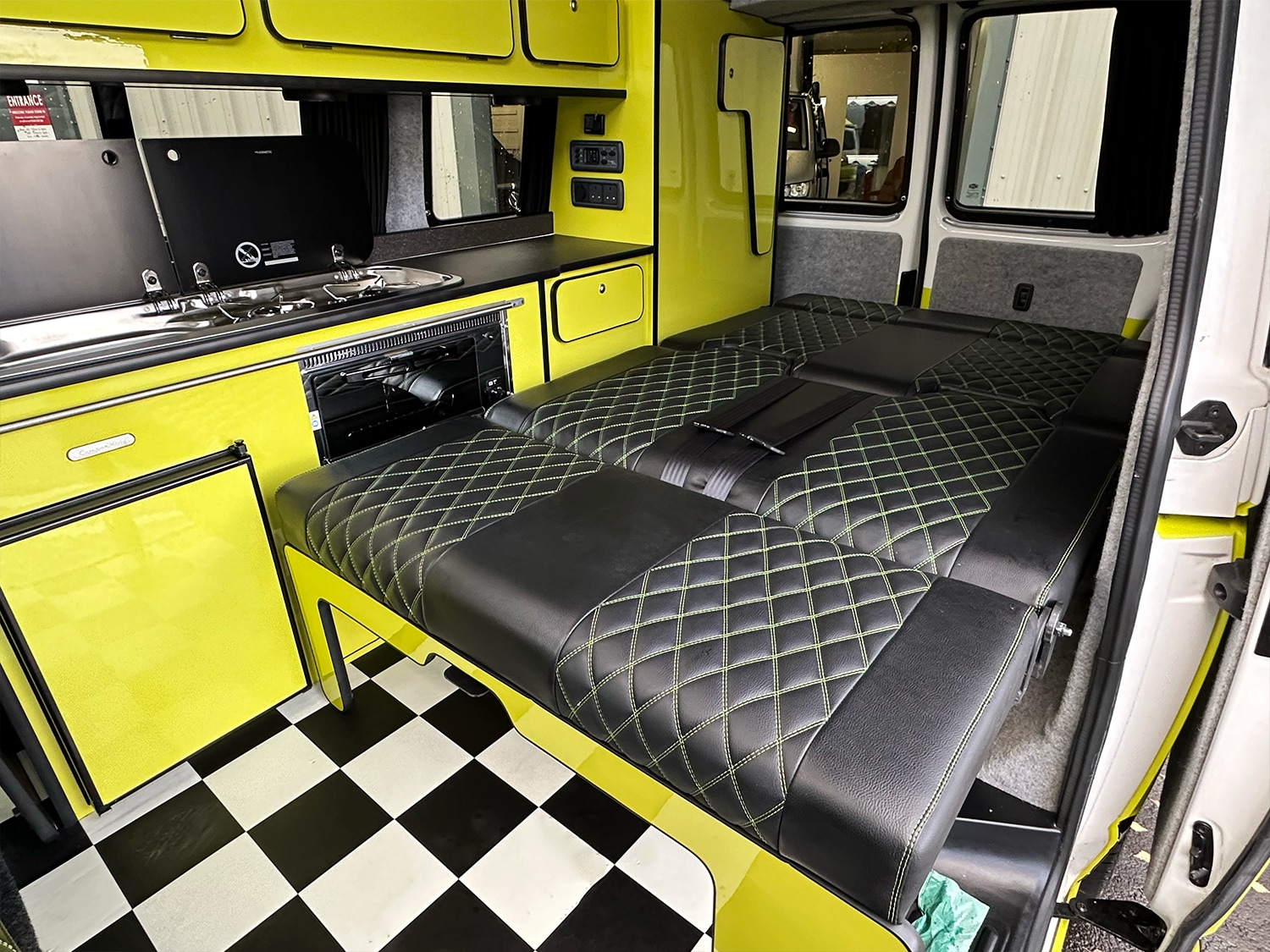 Inside a custom rv rental: bright yellow camper van interior with modern kitchen, checkerboard floor, and diamond-stitched bed.. Volkswagen Transporter T6.1 CamperKing Monte Carlo 2020