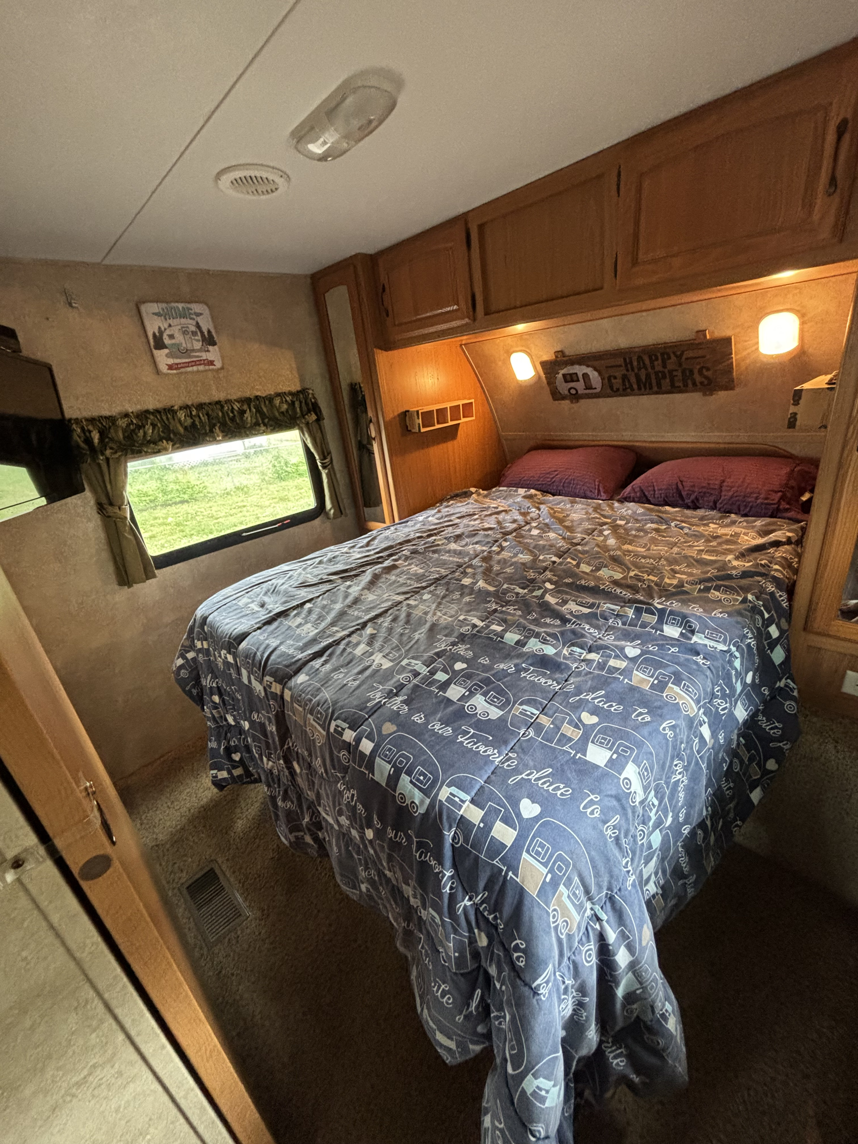 Cozy RV rental bedroom featuring a comfy bed with a camper-themed comforter and "Happy Campers" sign.. Keystone RV Laredo 2011