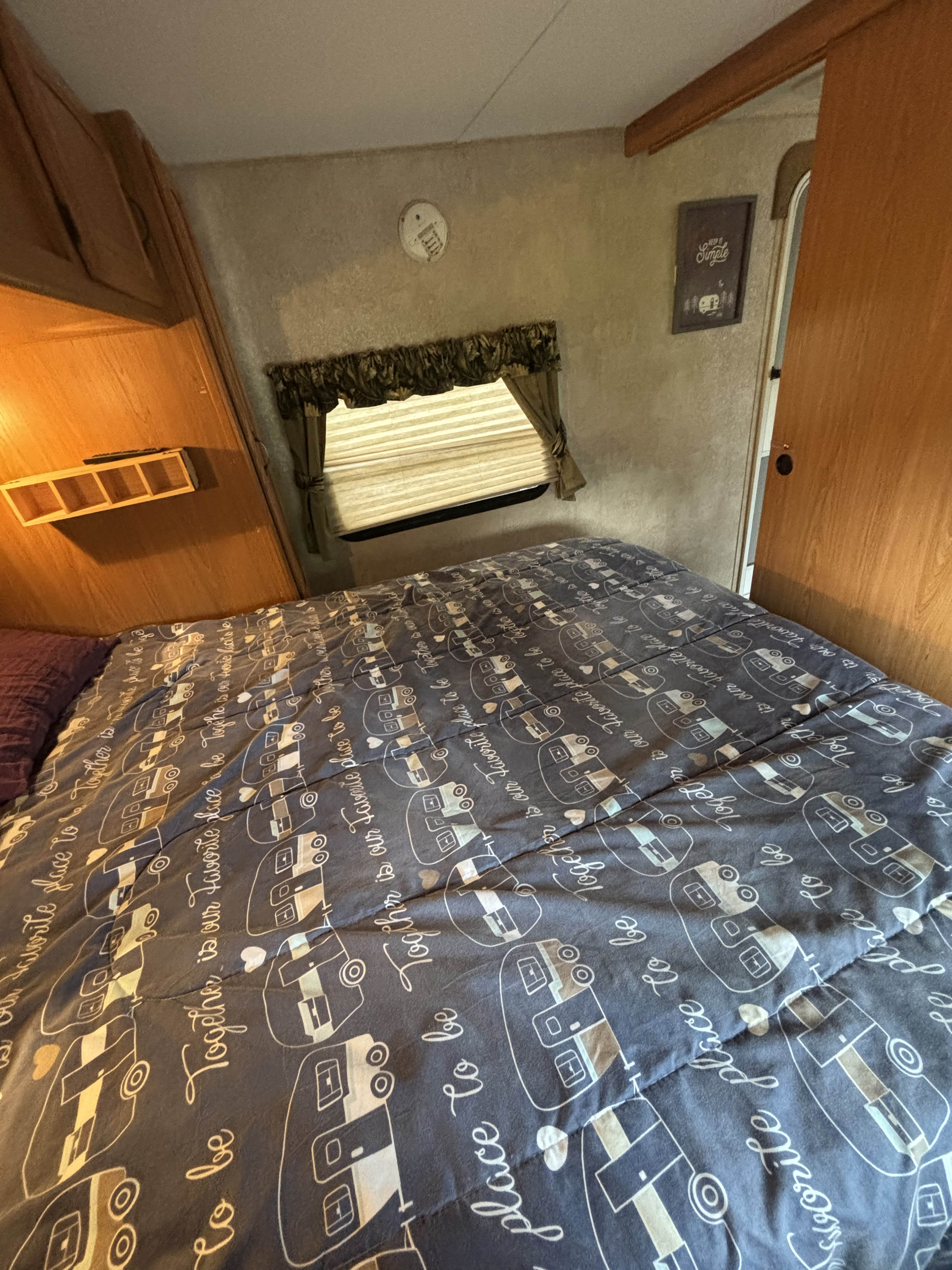 Cozy rv rental bedroom features a bed with "Together is our favorite place to be" comforter, window, and wood interior.. Keystone RV Laredo 2011