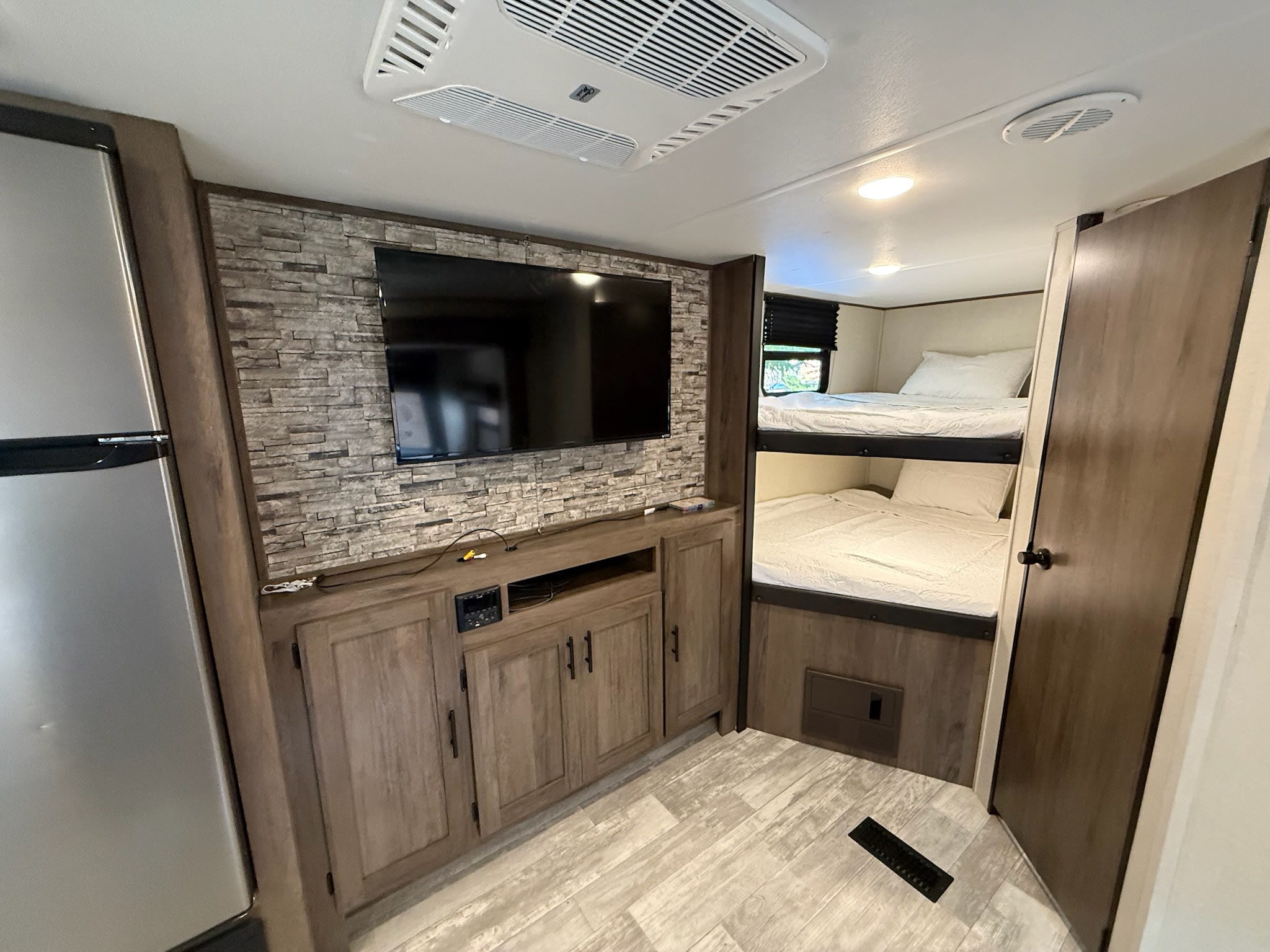 This RV rental interior showcases a TV entertainment center, a fridge, and comfortable bunk beds, ideal for family travel.. Forest River Primetime Avenger 27dbs 2021