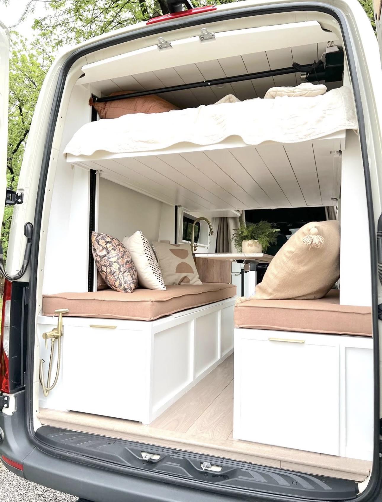 Inside this modern RV rental: a custom camper van featuring an elevated bed, lounge seating, and built-in kitchen.. Mercedes-Benz Sprinter 2021