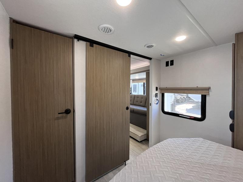 Modern RV rental interior: bedroom in foreground, with a sliding door to the main living space. Great for travel adventures!. Wildwood X-Lite 25ICE 2025