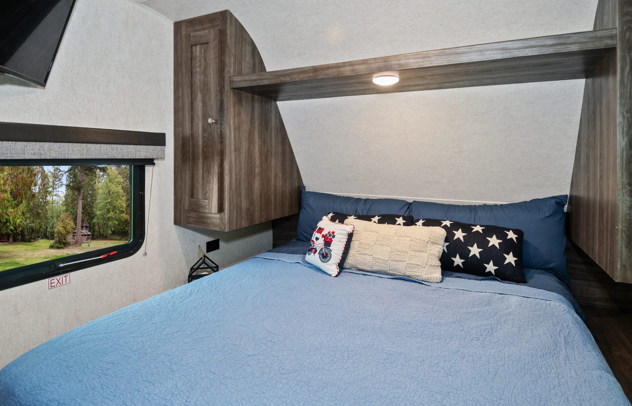 This comfortable RV rental bedroom features a cozy bed with decorative pillows and a serene view of nature.. Highland Ridge RV Open Range 2019