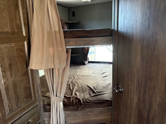 RV rental interior: bunk beds with light brown privacy curtains and wood-look walls. Lower bunk shows a dark blanket for comfort.. Keystone RV Cougar 28RBS 2016