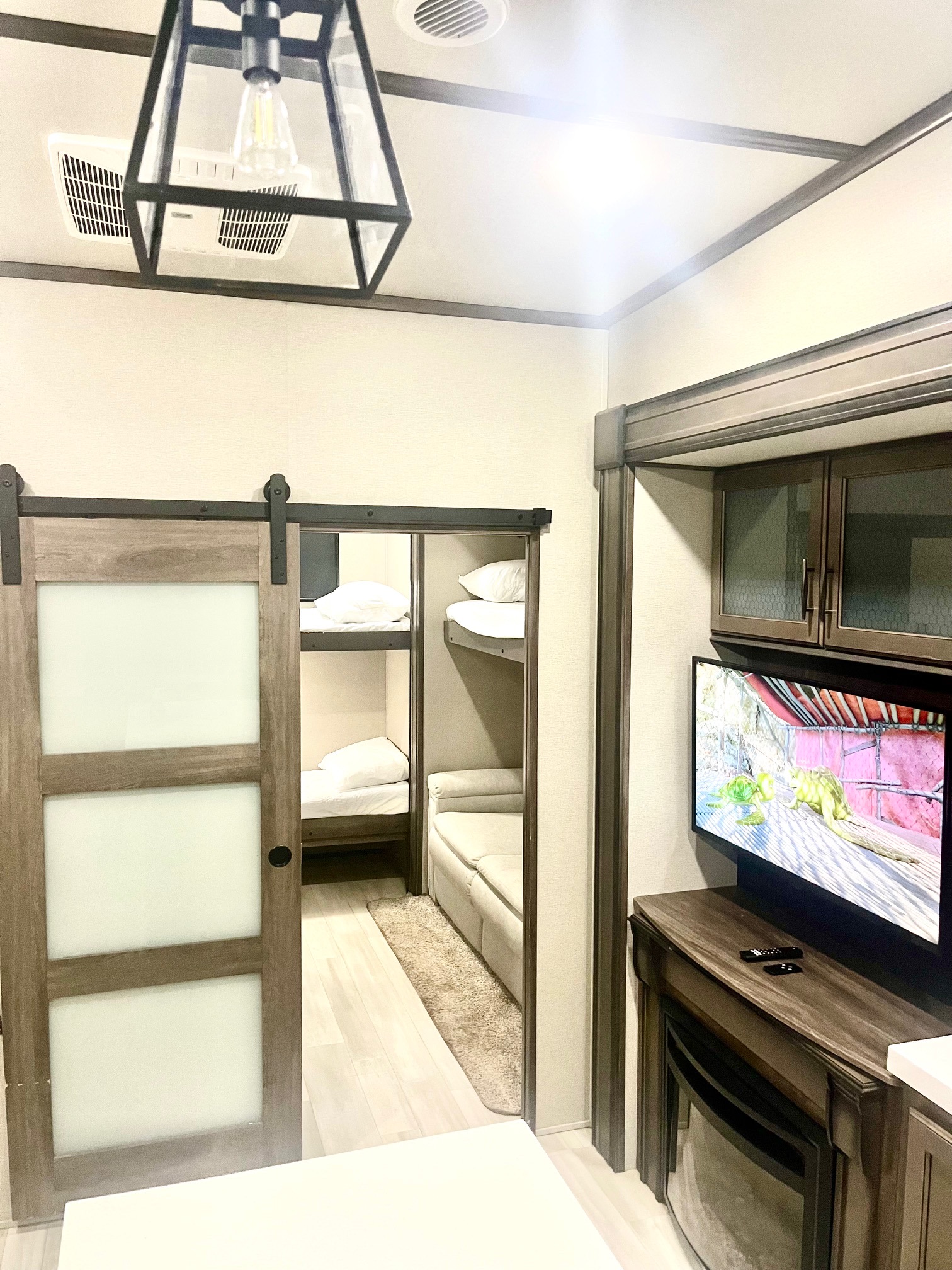 Modern rv rental interior featuring a bunk room with a sliding barn door, TV, and electric fireplace for compact living.. Grand Design Solitude 2021