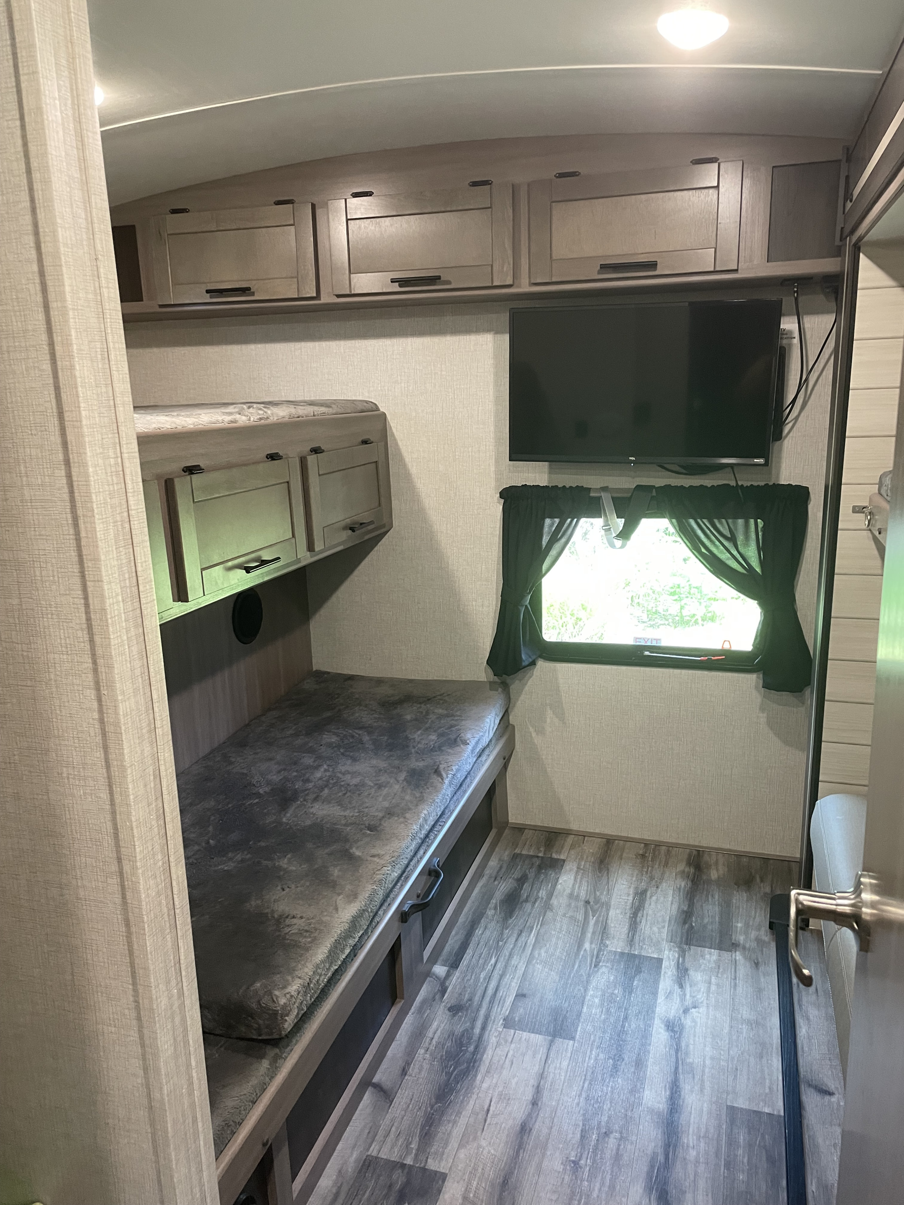 RV rental bunk room with lower bed, overhead cabinets, mounted TV, and window. Designed for comfort.. Crossroads RV Sunset Trail Super Lite 2023