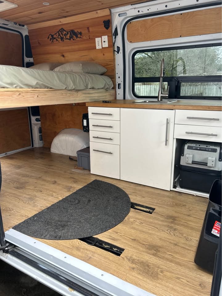 RV rental ready: Interior view of a comfortable camper van featuring a raised bed, kitchen, and wood accents.. RAM ProMaster 1500 2017