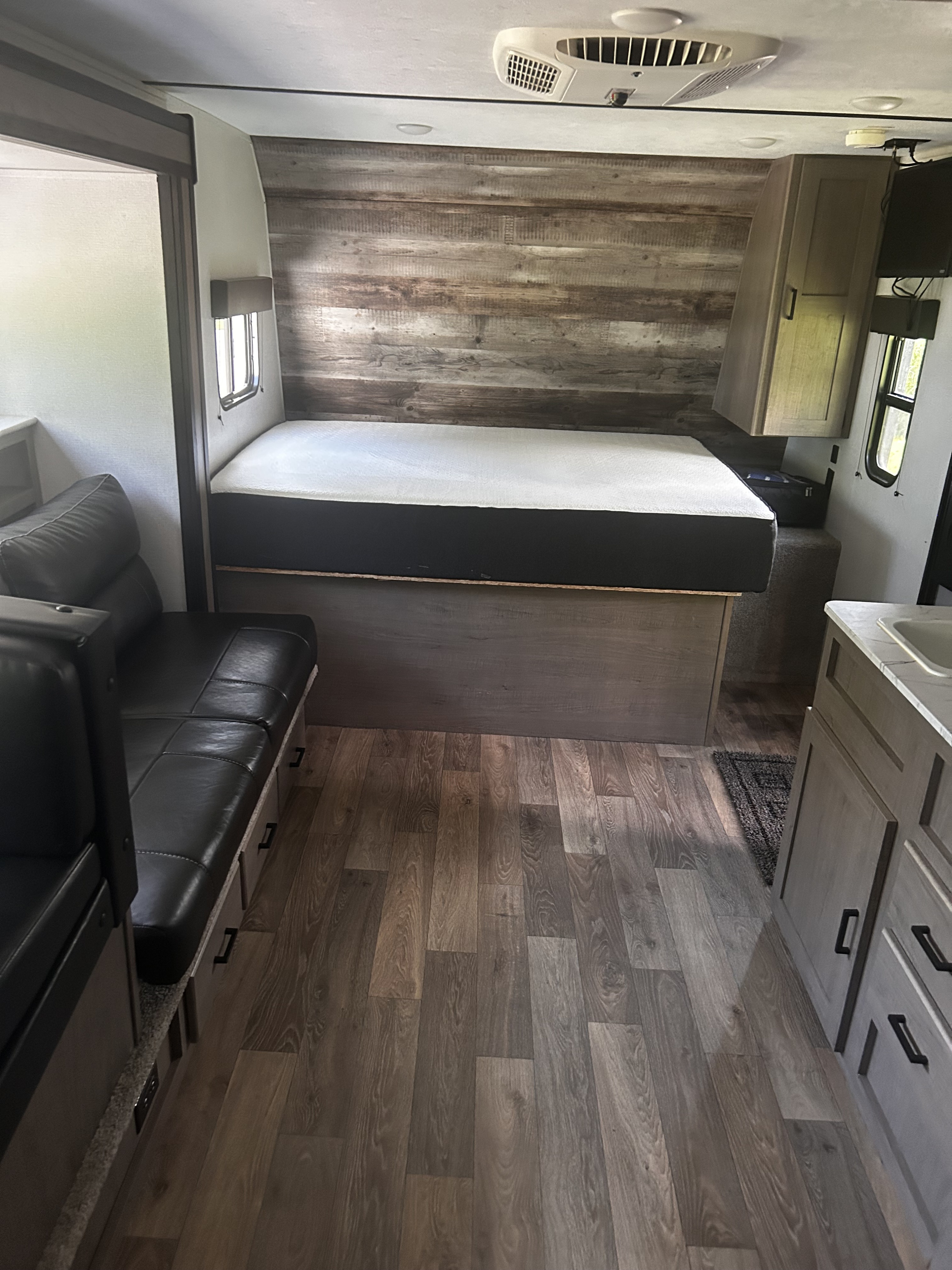 Modern RV rental interior with a comfortable bed, black dinette seating, and wood-look flooring, designed for comfort.. Keystone RV Hideout 2020