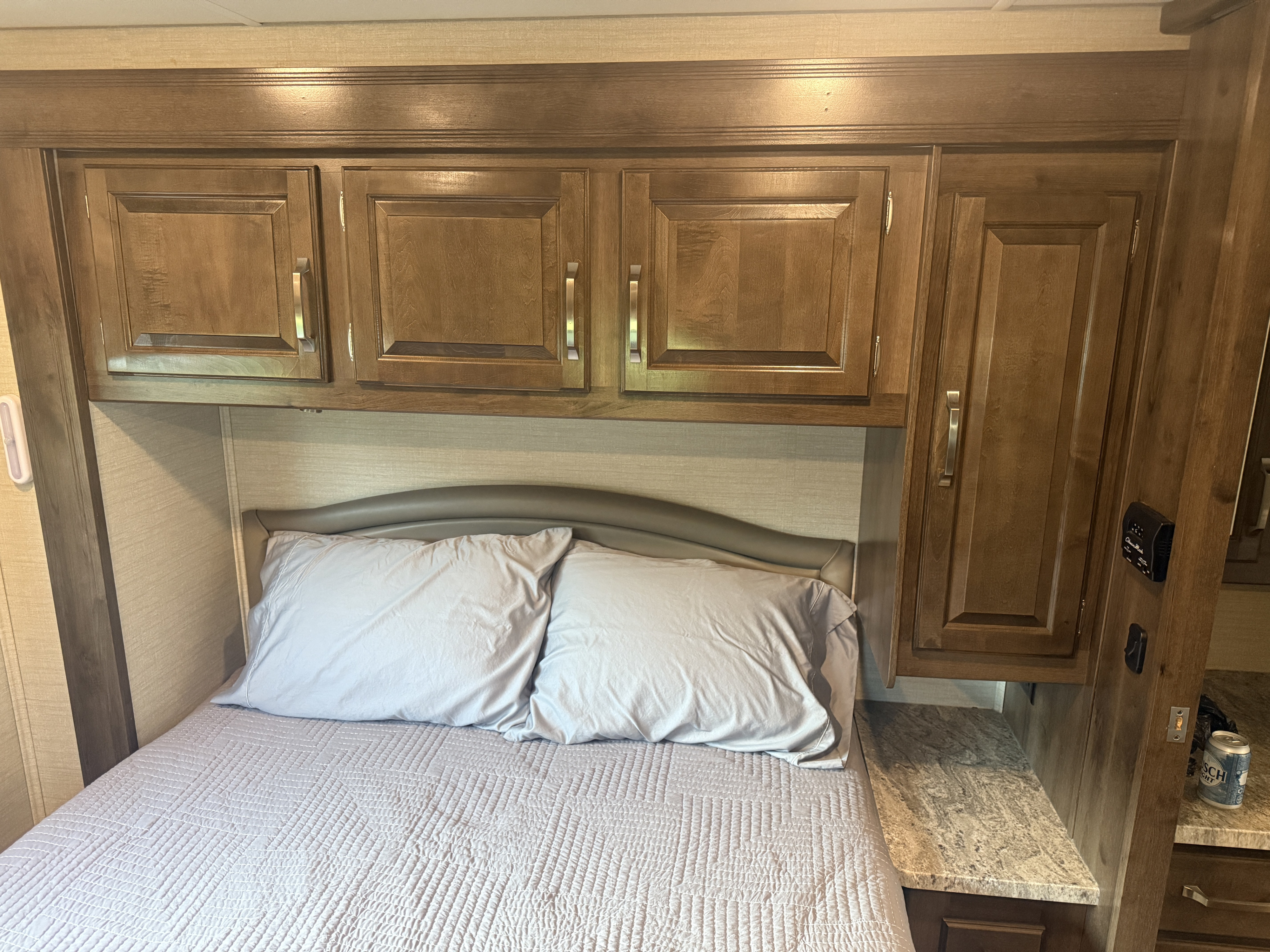 Cozy RV rental bedroom features a comfy bed with light bedding, overhead cabinets, and a compact bedside table.. Jayco Greyhawk 2018