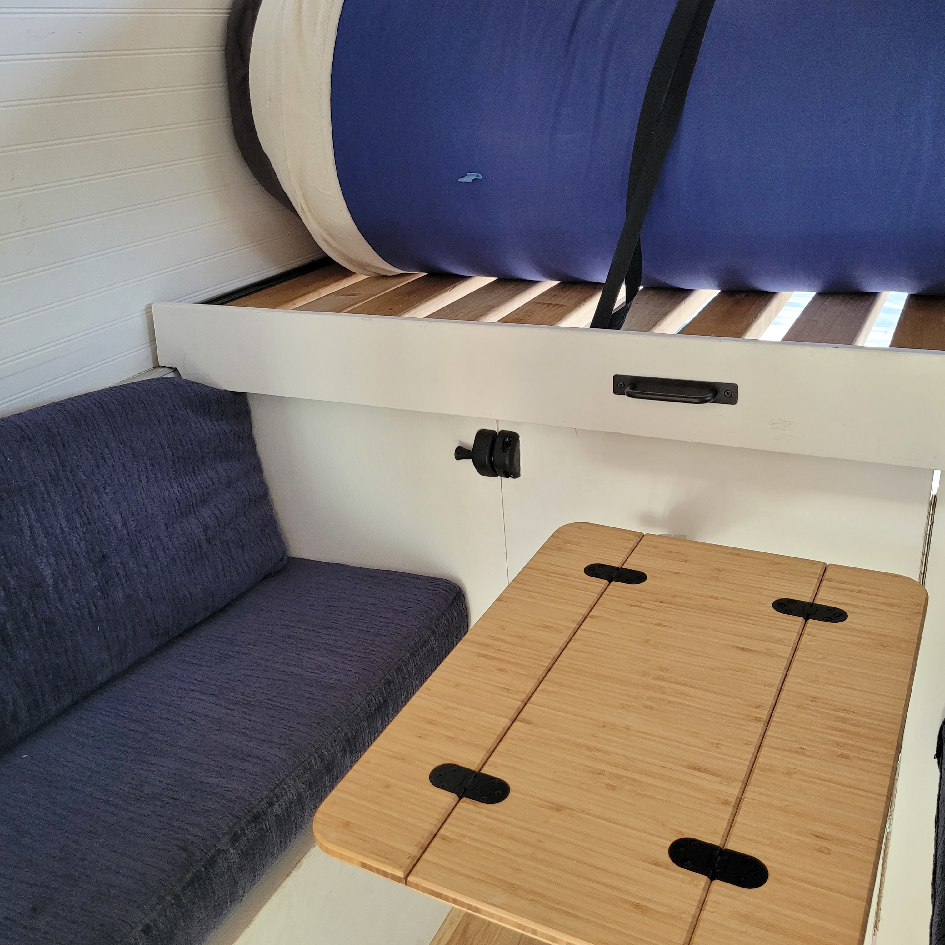 Compact RV rental interior with blue cushioned seating, a fold-out bamboo table, and a raised sleeping area above.. Dodge Sprinter Van 2003