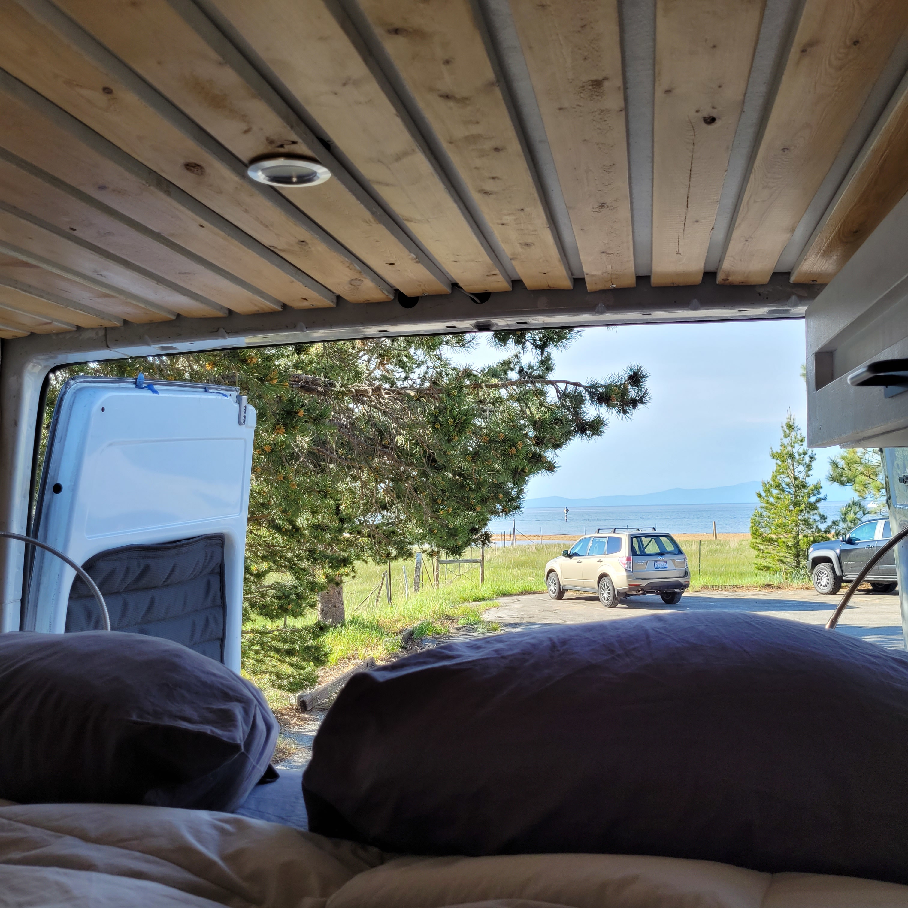 Serene RV rental view from bed: Lake, trees, parked cars, & distant mountains.. Dodge Sprinter Van 2003