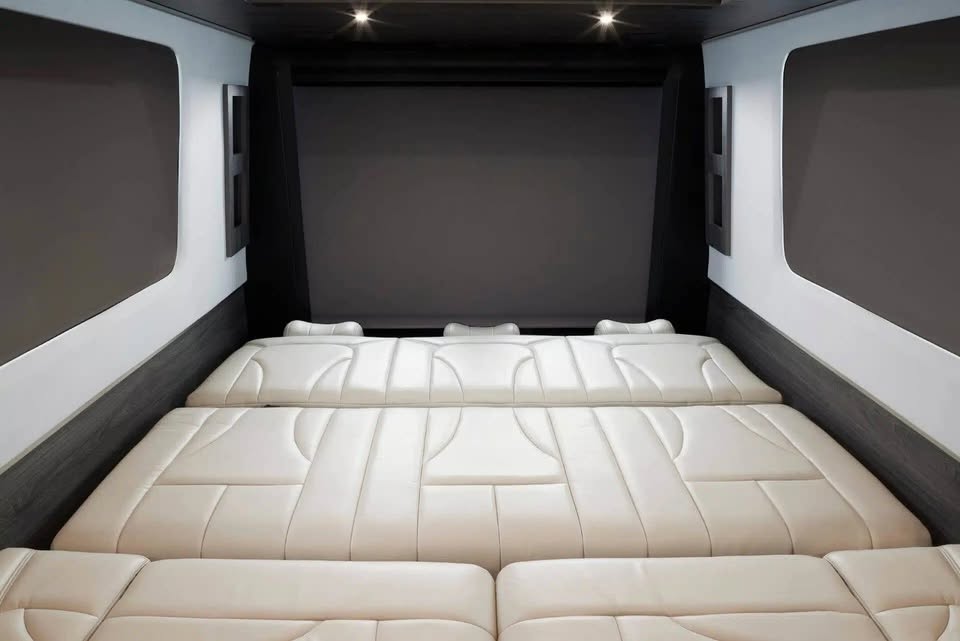 Luxurious RV rental interior: a large, light-colored convertible bed/seating setup with sleek walls and overhead lights.. Grech RV Strada-ion 2023
