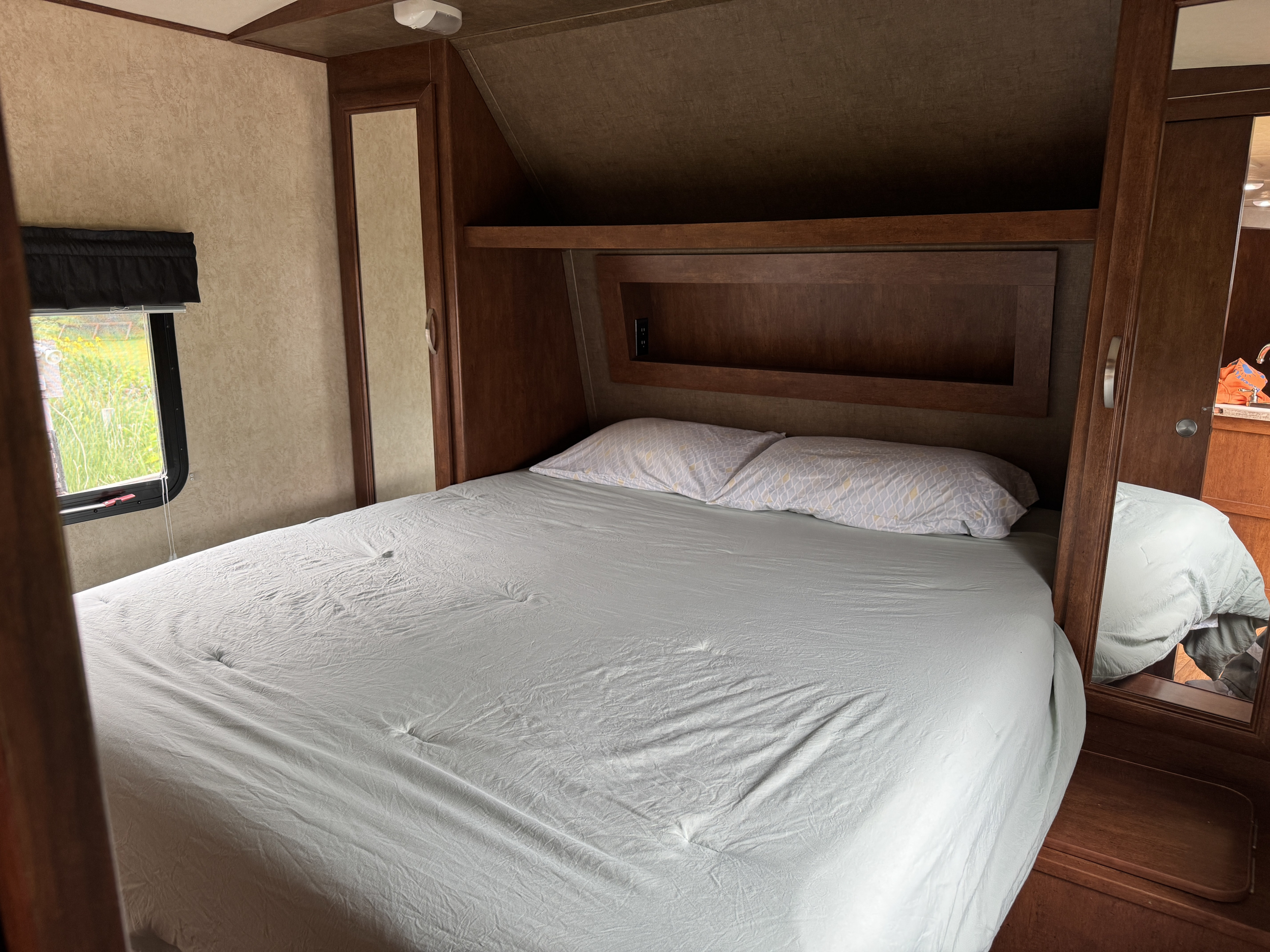 Comfortable RV rental bedroom with a cozy bed, window view of greenery, and wood accents. Ideal for relaxing on your trip.. Forest River Vibe Extreme Lite 2015