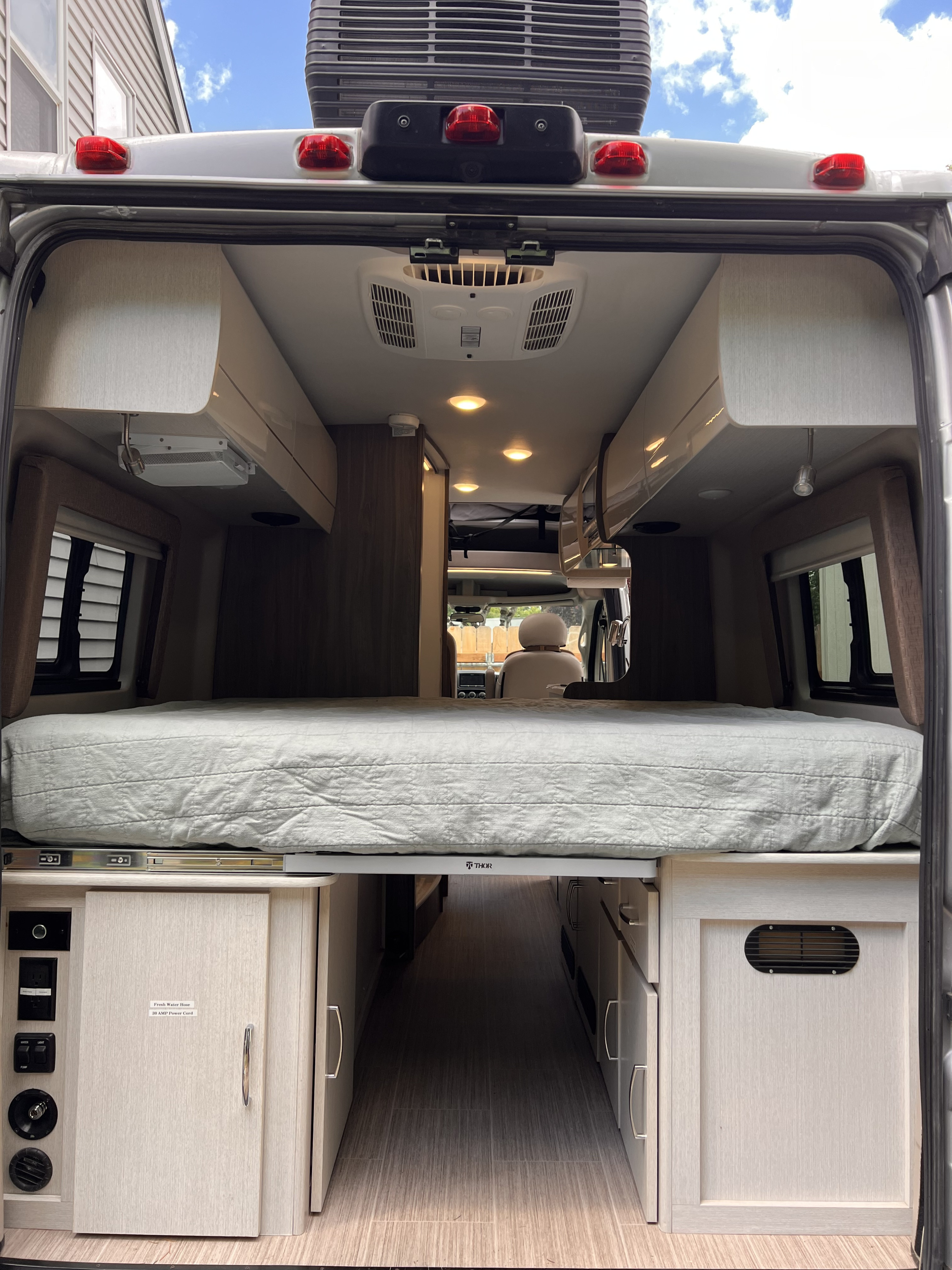 RV rental: View of the camper's spacious interior looking forward, featuring a raised bed, central aisle, and controls.. Thor Tellaro 2022
