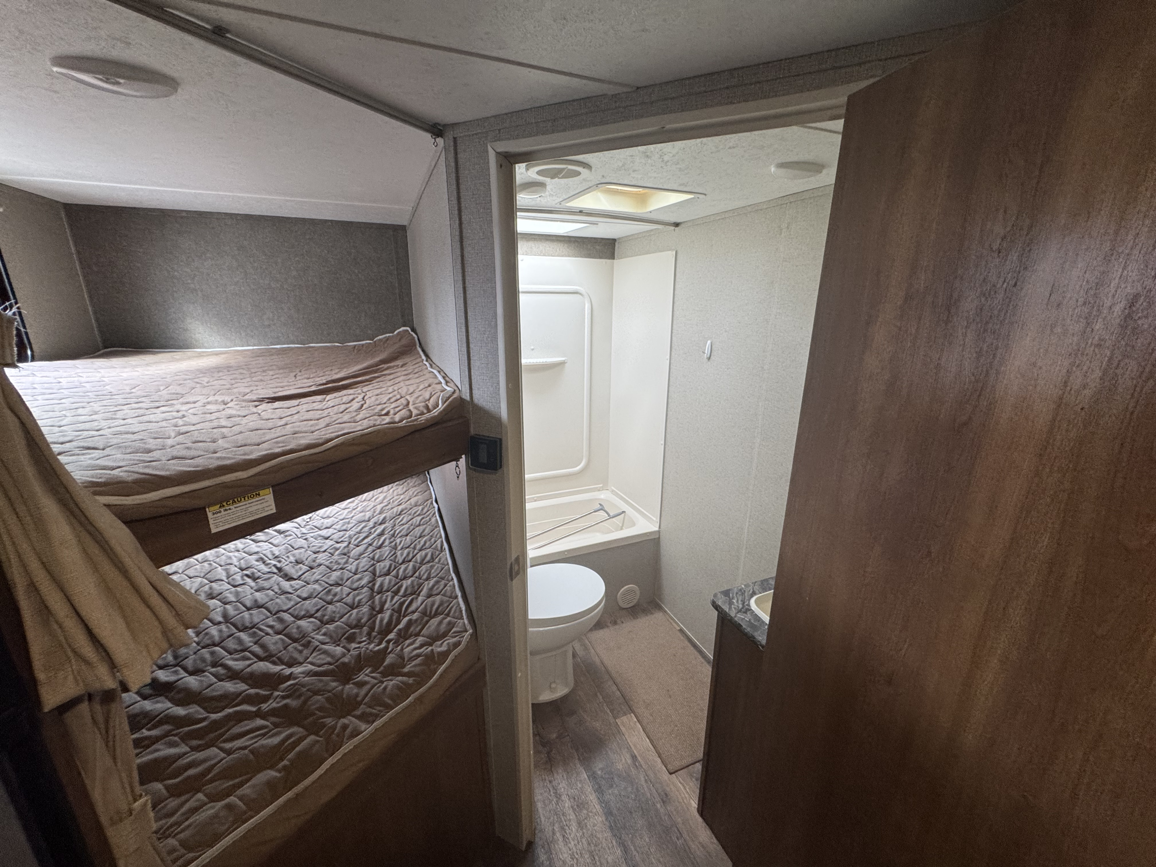 Compact RV rental interior featuring cozy bunk beds and a functional bathroom with a tub, toilet, and sink.. Keystone RV Springdale 2018