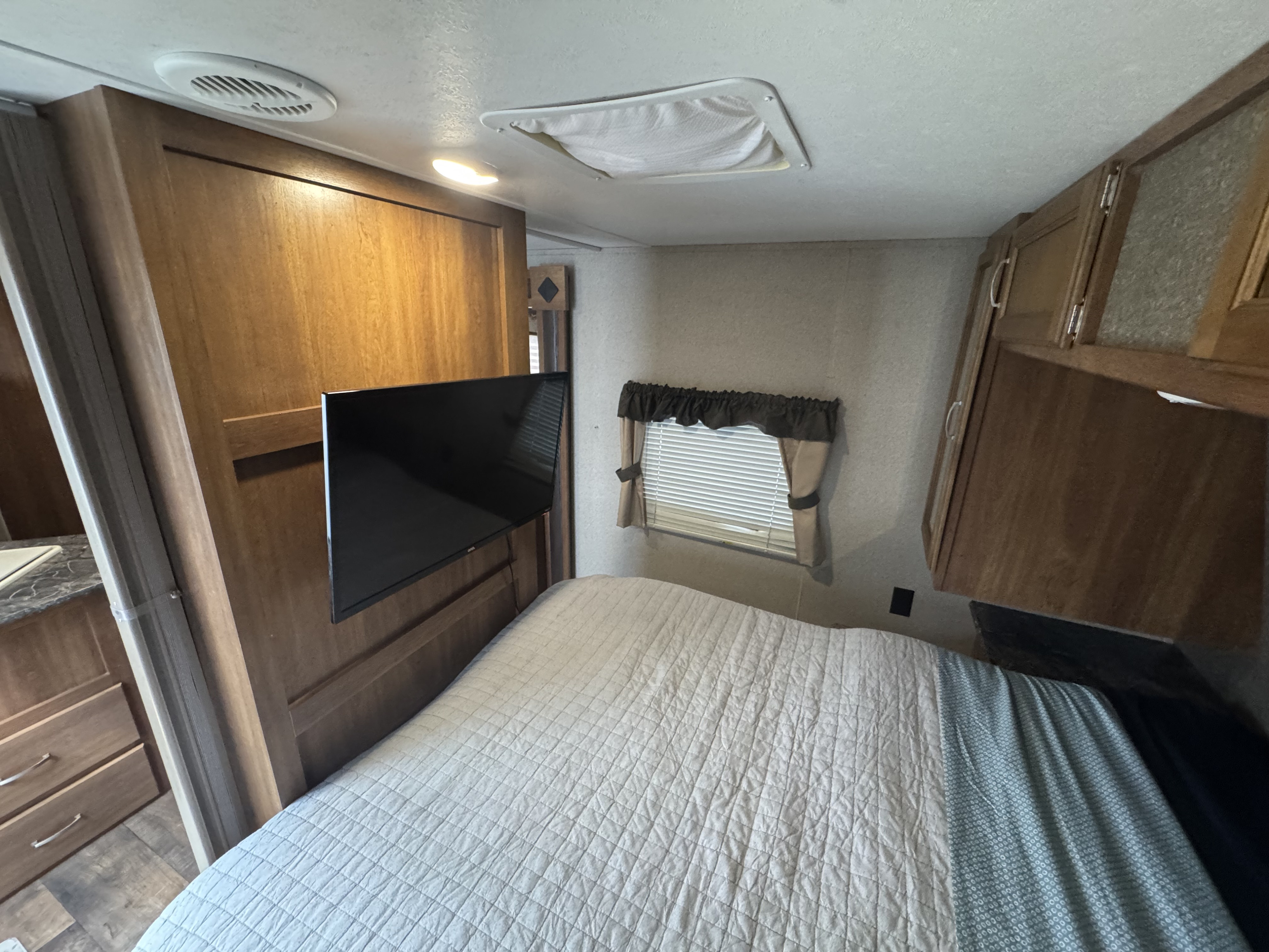 Cozy RV rental bedroom features a comfy bed, wall-mounted TV, window with blinds, and ample wood cabinets.. Keystone RV Springdale 2018