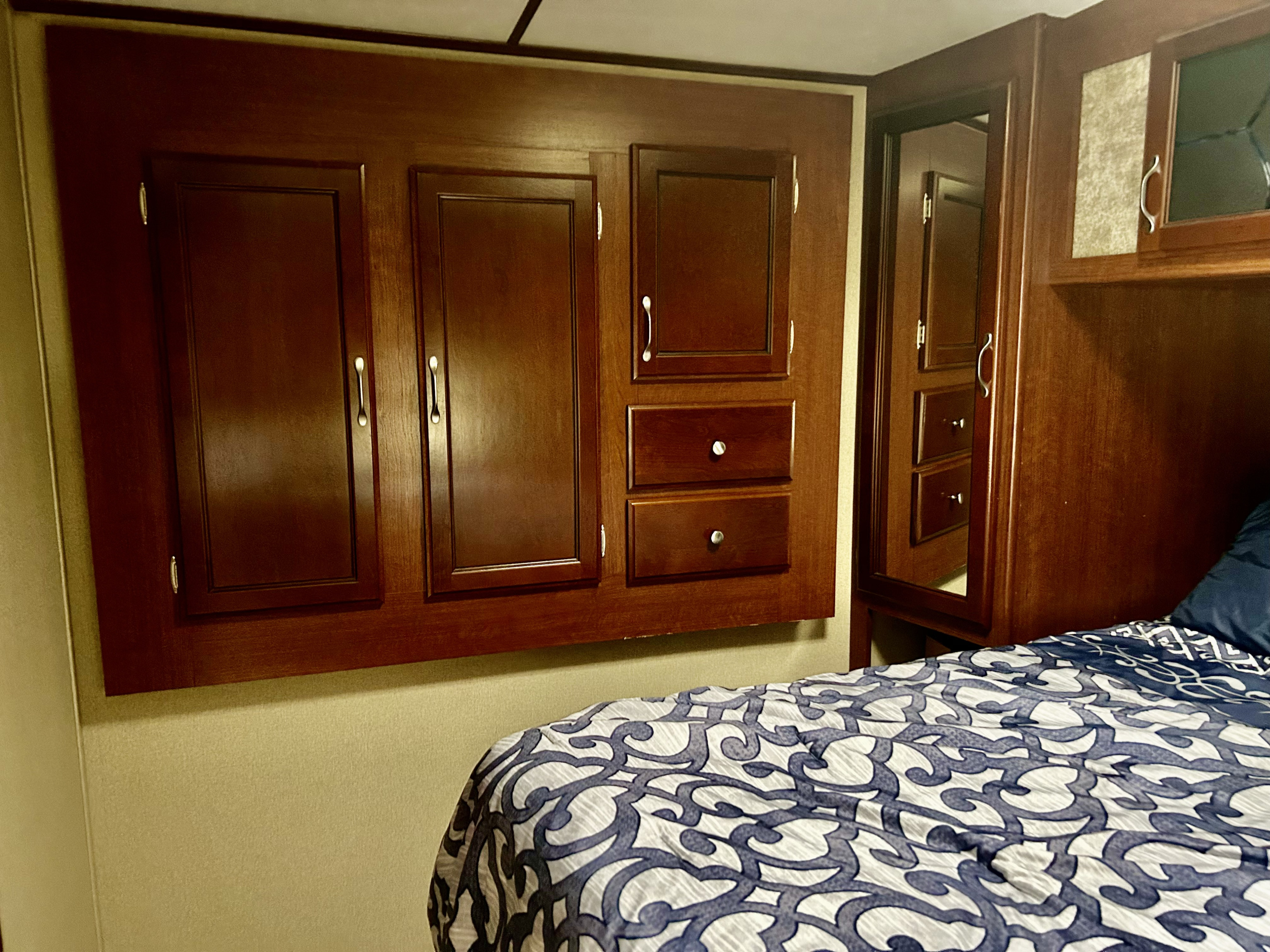 Inside an RV rental bedroom with dark wood cabinets, drawers, a mirror, and a bed with blue and white patterned bedding.. Evergreen Sunvalley 2015