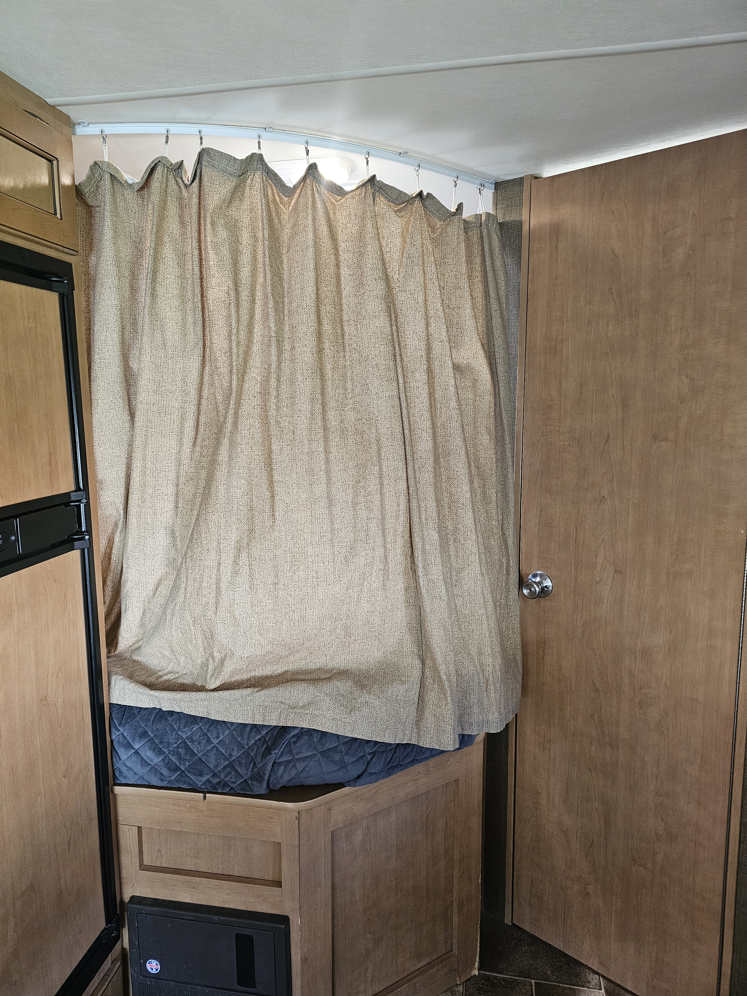 **RV rental** interior: Bed with blue quilt, privacy curtain, fridge, electrical panel, and wooden door.. Thor Four Winds 2016