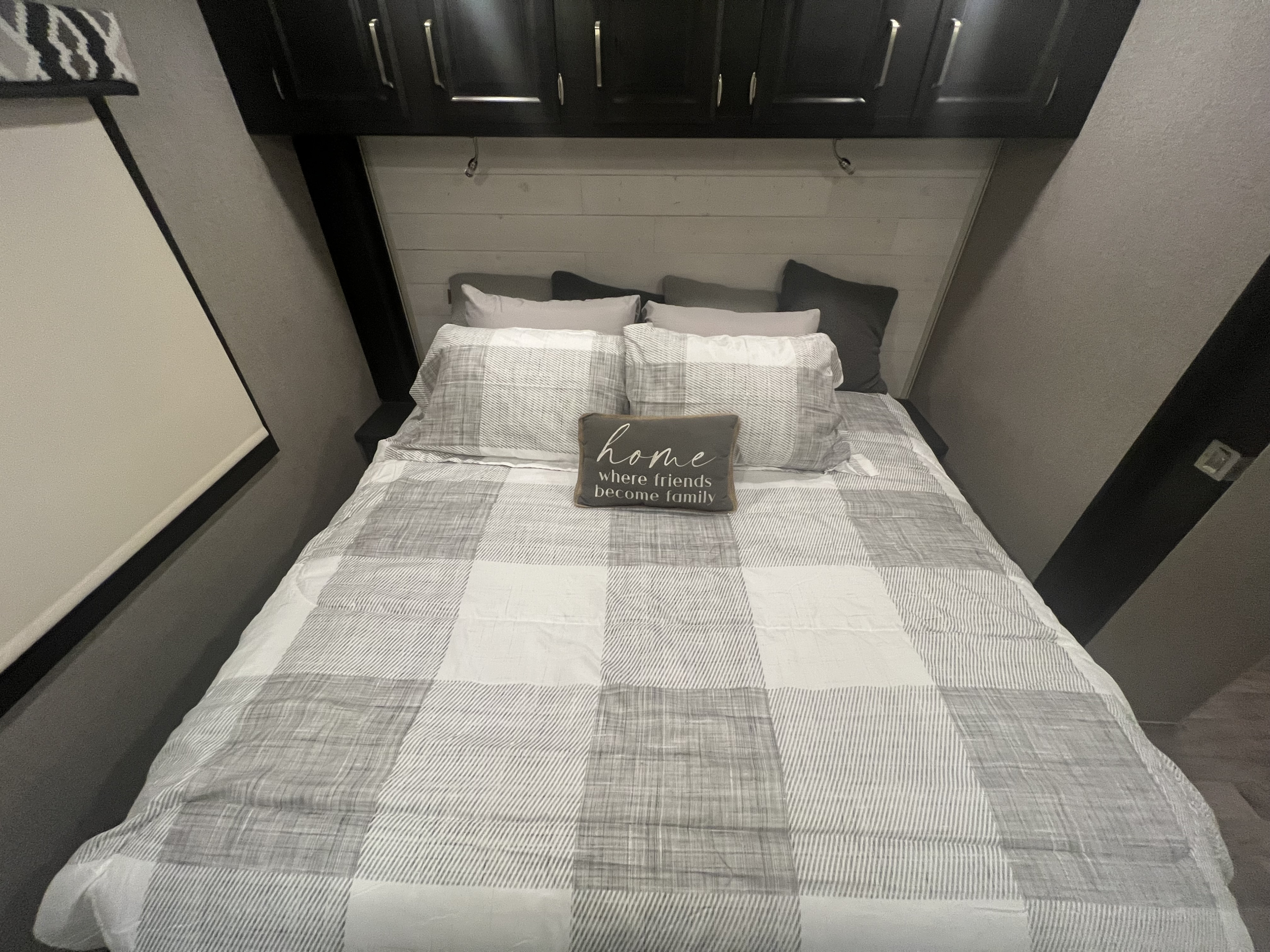 Experience comfort in this **rv rental** bedroom: a full bed with gray & white plaid bedding, dark overhead cabinets, and a cozy pillow.. Jayco Precept 2021