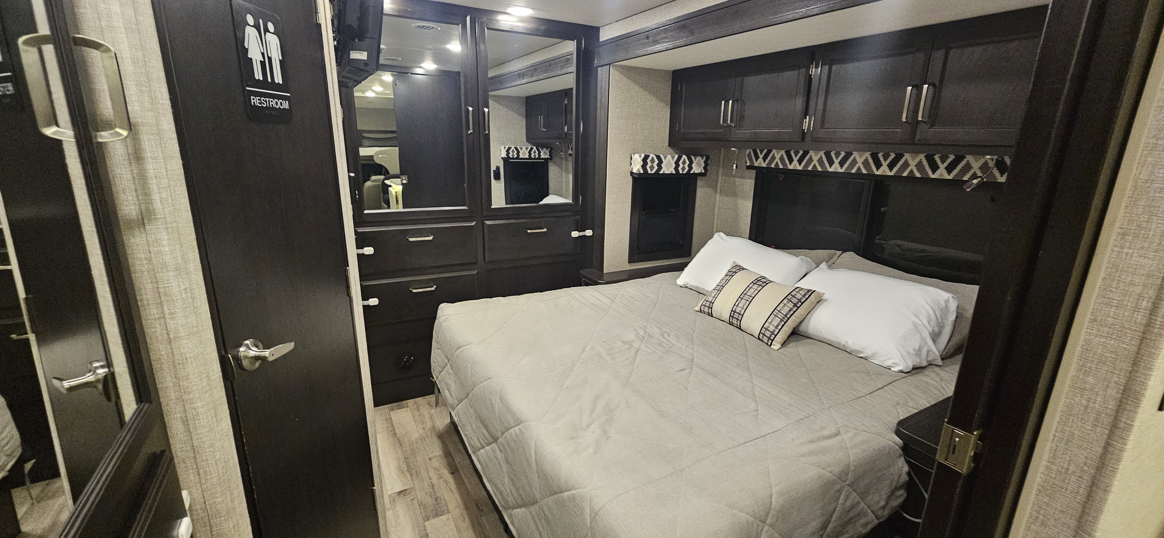 RV rental: Modern motorhome bedroom with a bed, dark wood storage, and a restroom door on the left.. Jayco Greyhawk 2022