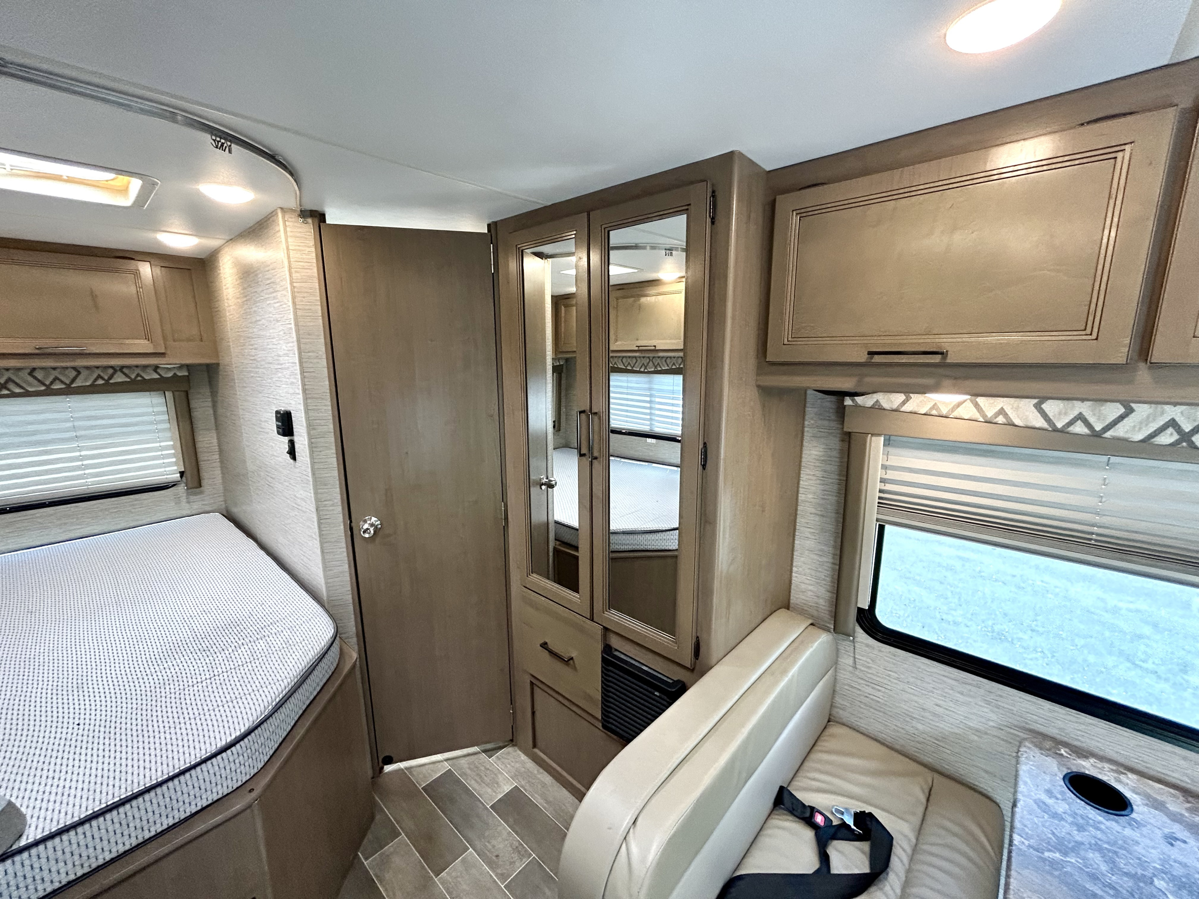 RV rental interior showing a compact living area with a bed, mirrored wardrobe, dinette seating, and overhead cabinets.. Thor Quantum SE 2021