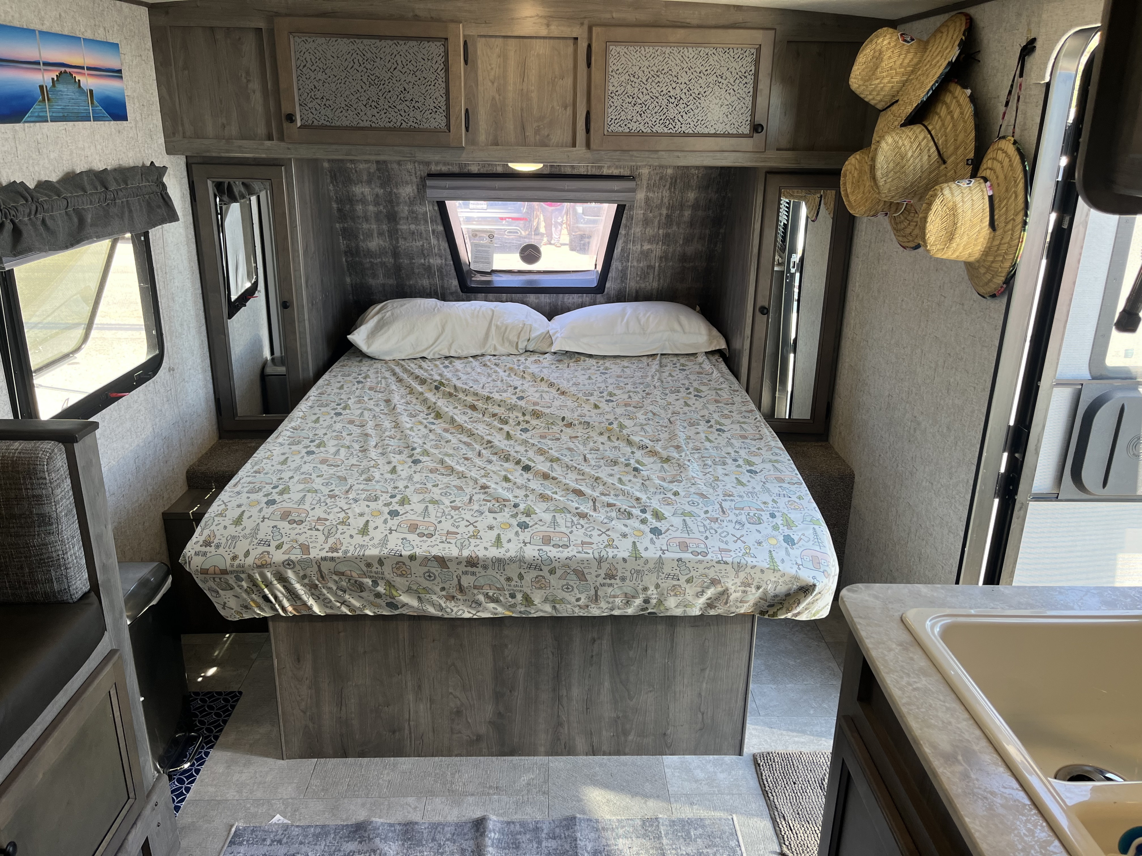 Cozy RV rental bedroom featuring a patterned bed, overhead cabinets, and practical built-in mirrors.. Coachmen Apex Nano 2019
