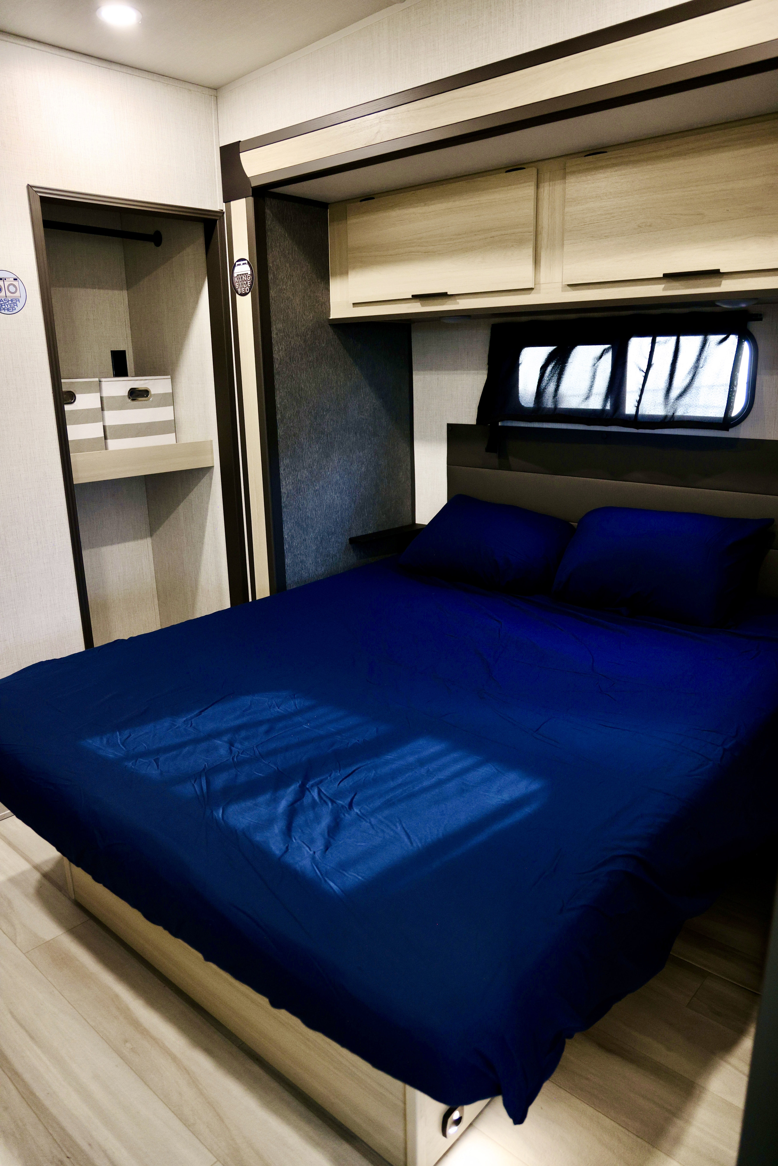 Explore this modern RV rental bedroom featuring a king-size bed, blue bedding, overhead cabinets, and a convenient closet.. Forest River Wildcat 2025