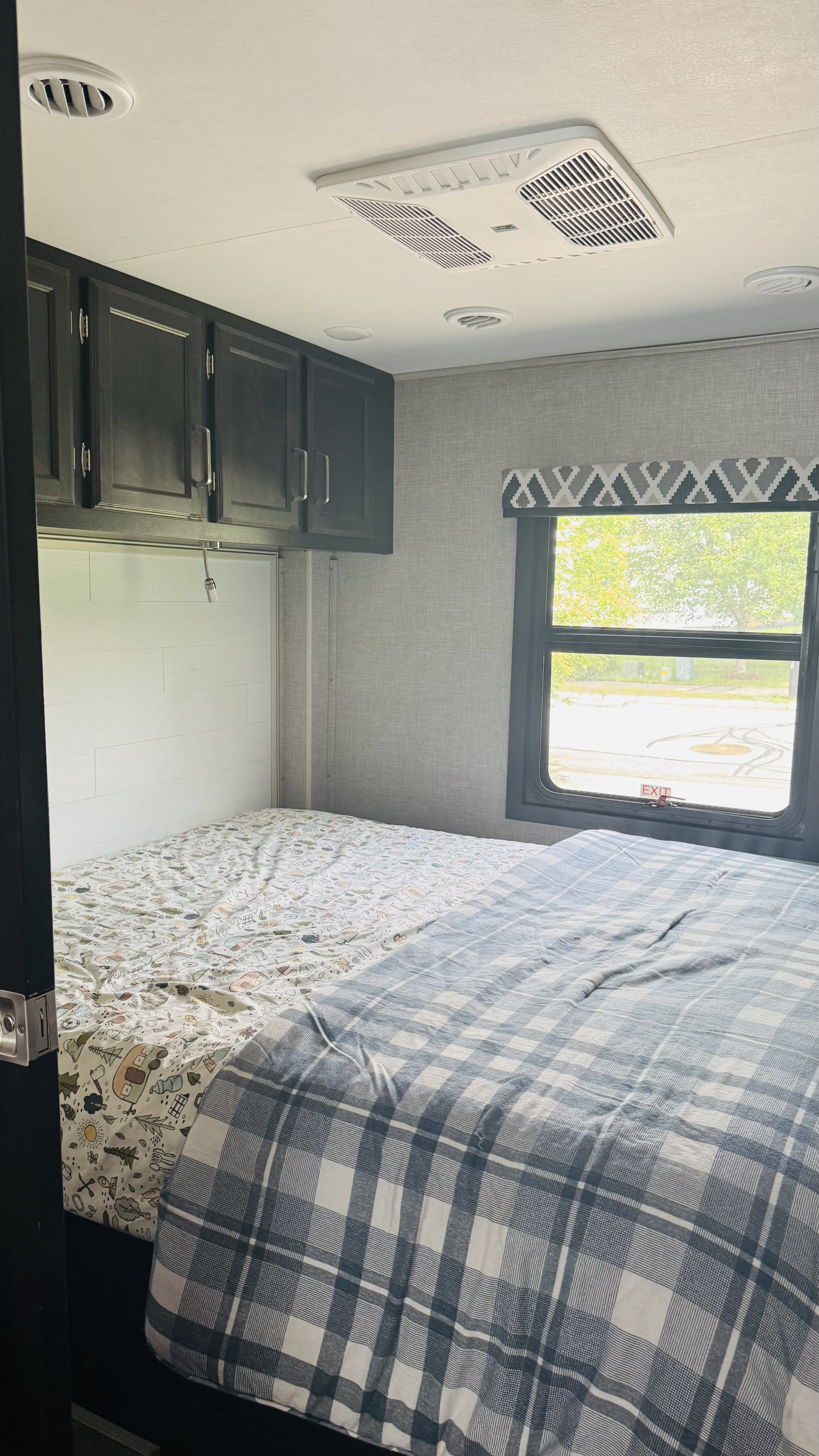 Cozy RV rental bedroom featuring a comfy bed with plaid and patterned bedding, overhead cabinets, and a window.. Jayco Alante 2022
