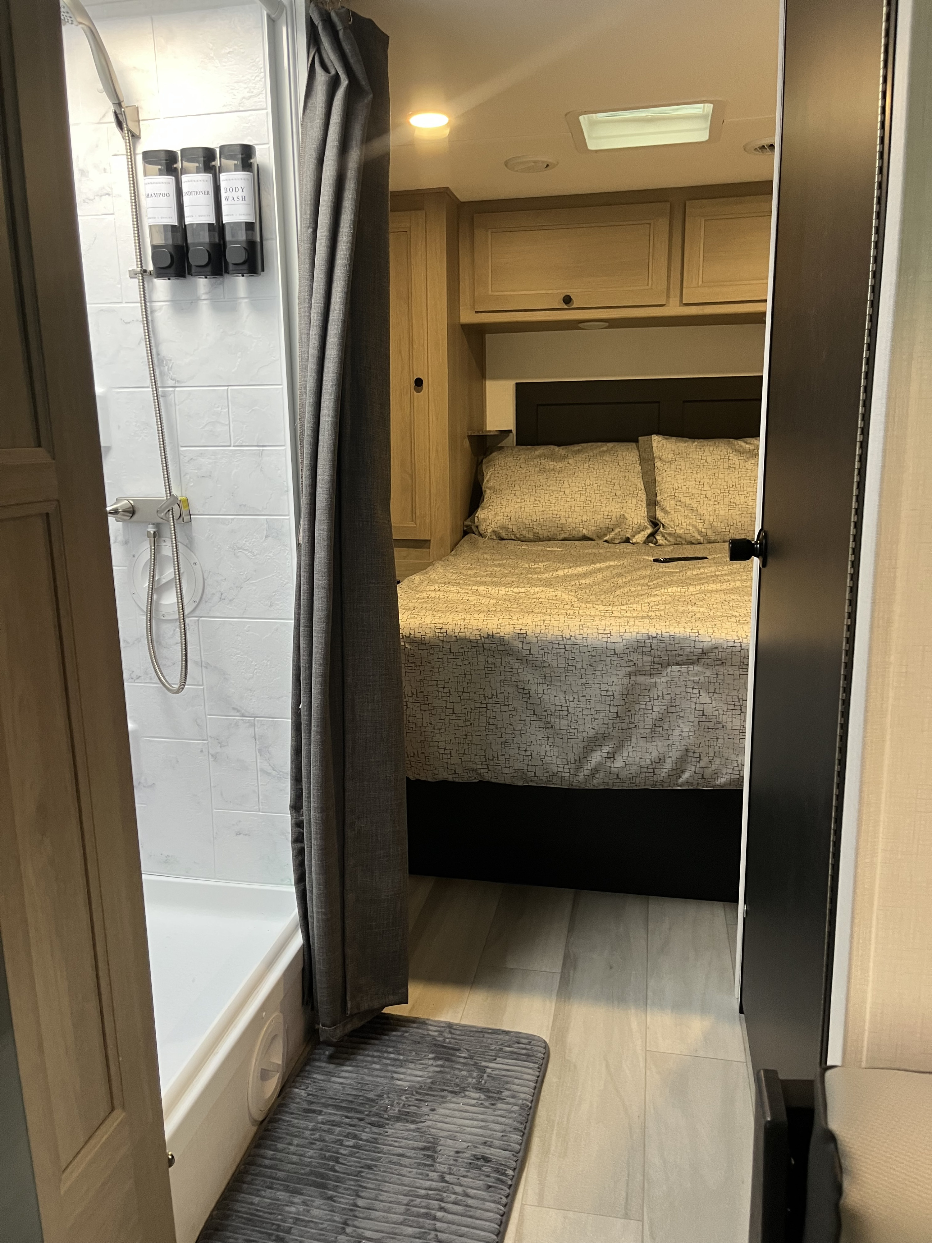 Cozy RV rental interior featuring a compact shower with amenity dispensers and a comfortable bedroom beyond.. Forest River Forester 2024