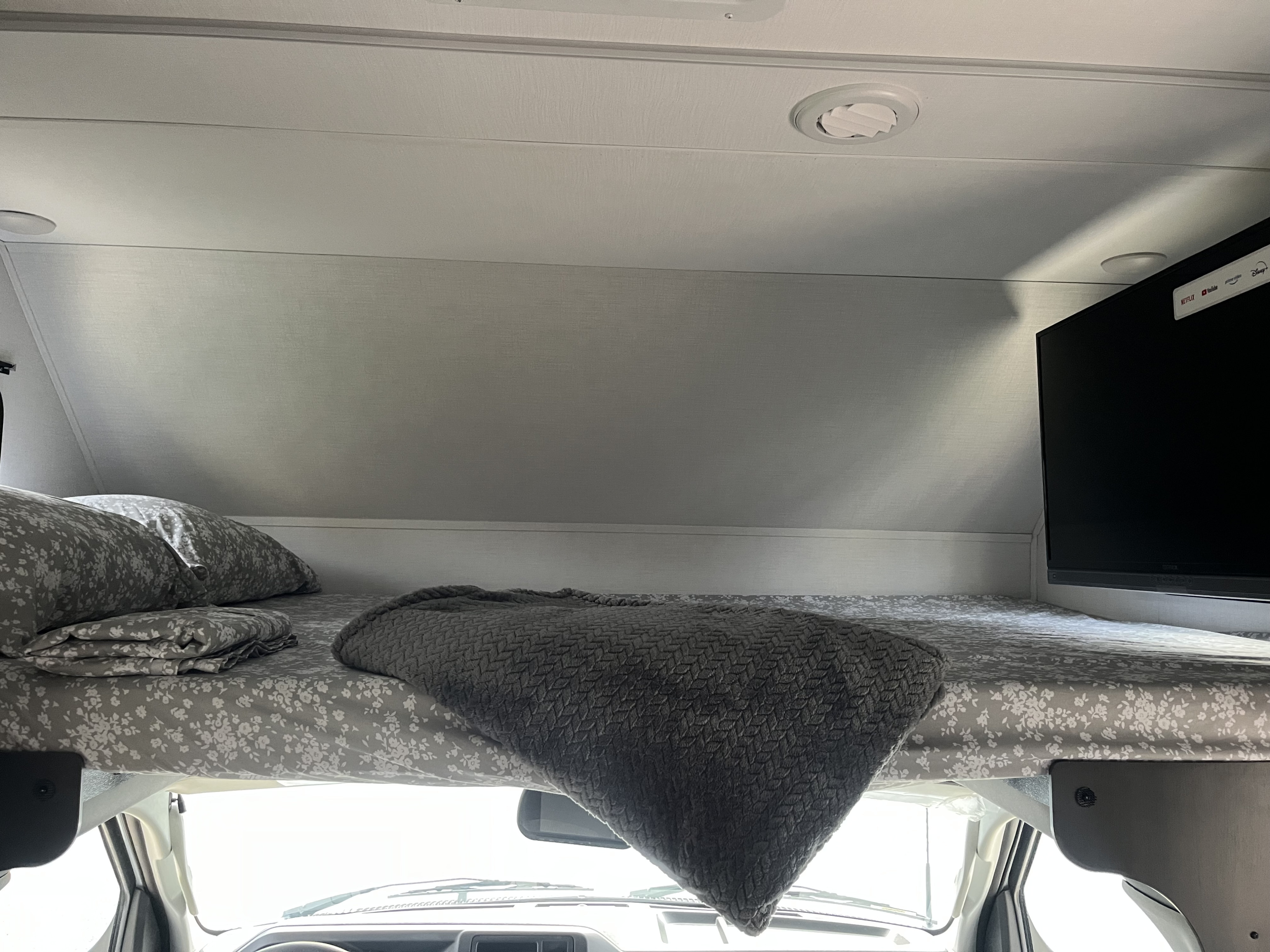 Cozy RV rental overhead sleeping area featuring a bed with patterned linens, pillows, a blanket, and a mounted TV.. Forest River Forester 2024