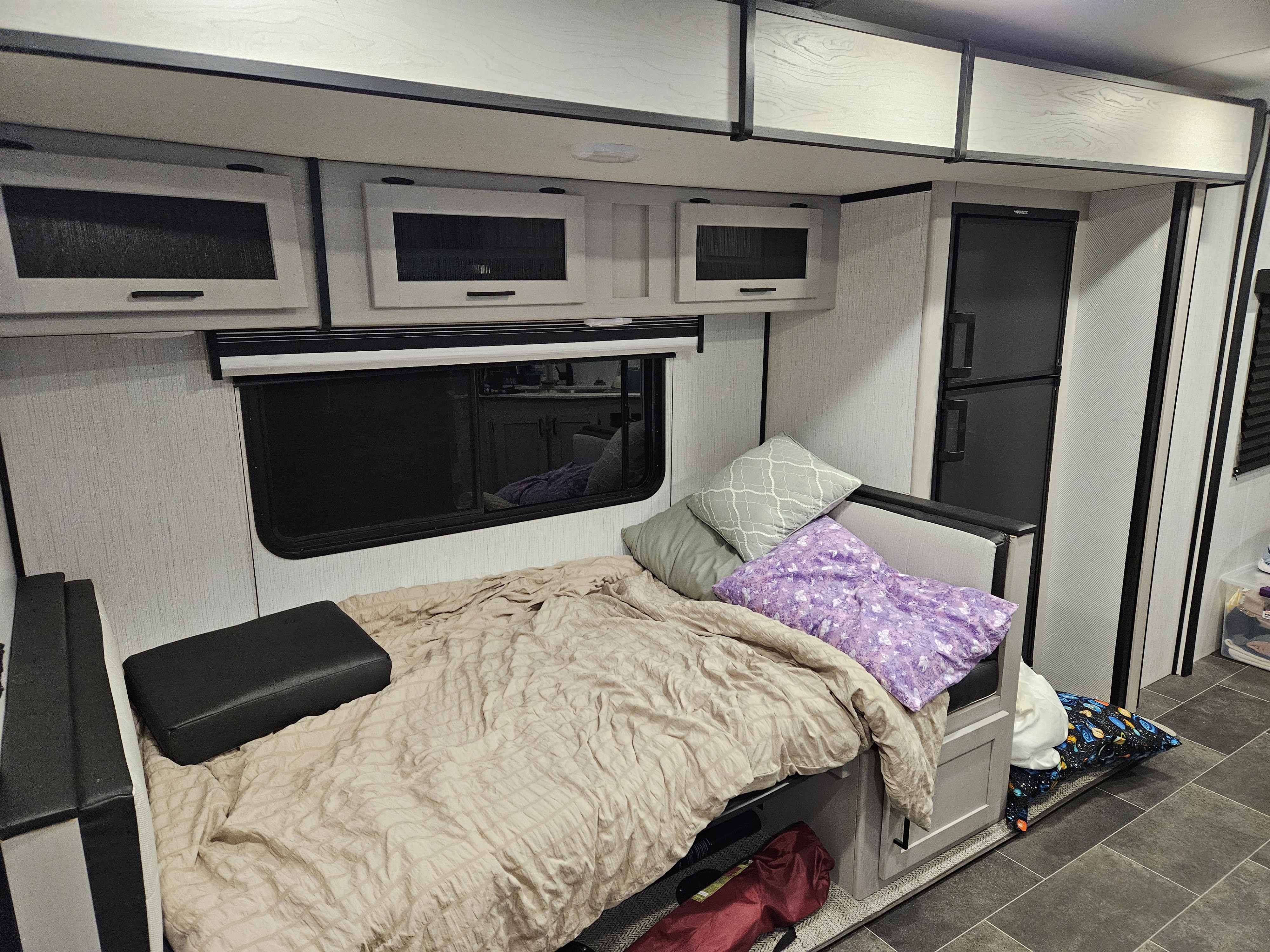 Cozy RV rental interior with a bed, pillows, window, overhead cabinets, and a refrigerator.. Heartland RVs Mallard 2022