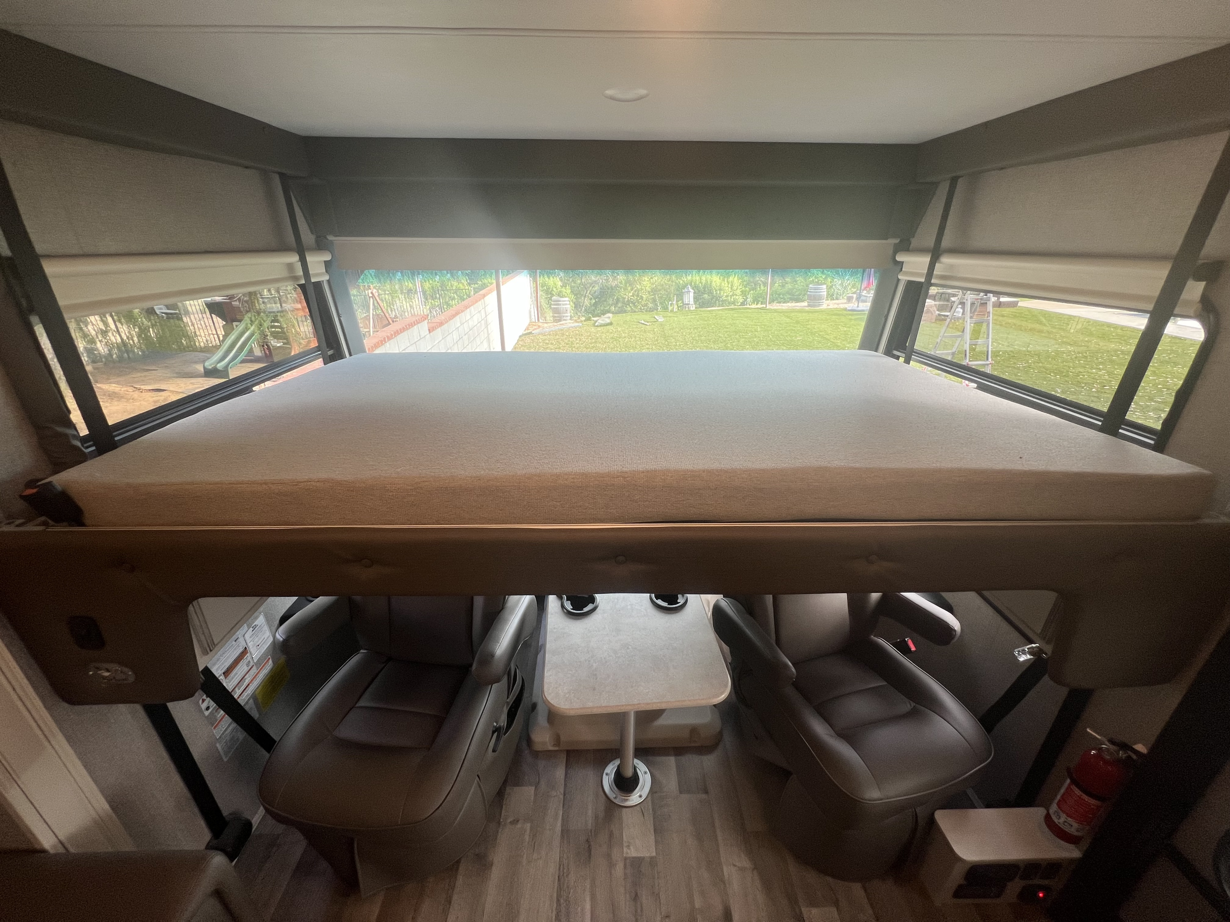 Inside an RV rental showing the cab-over bunk bed, front driver/passenger seats, and bright backyard view.. Jayco Precept 2021
