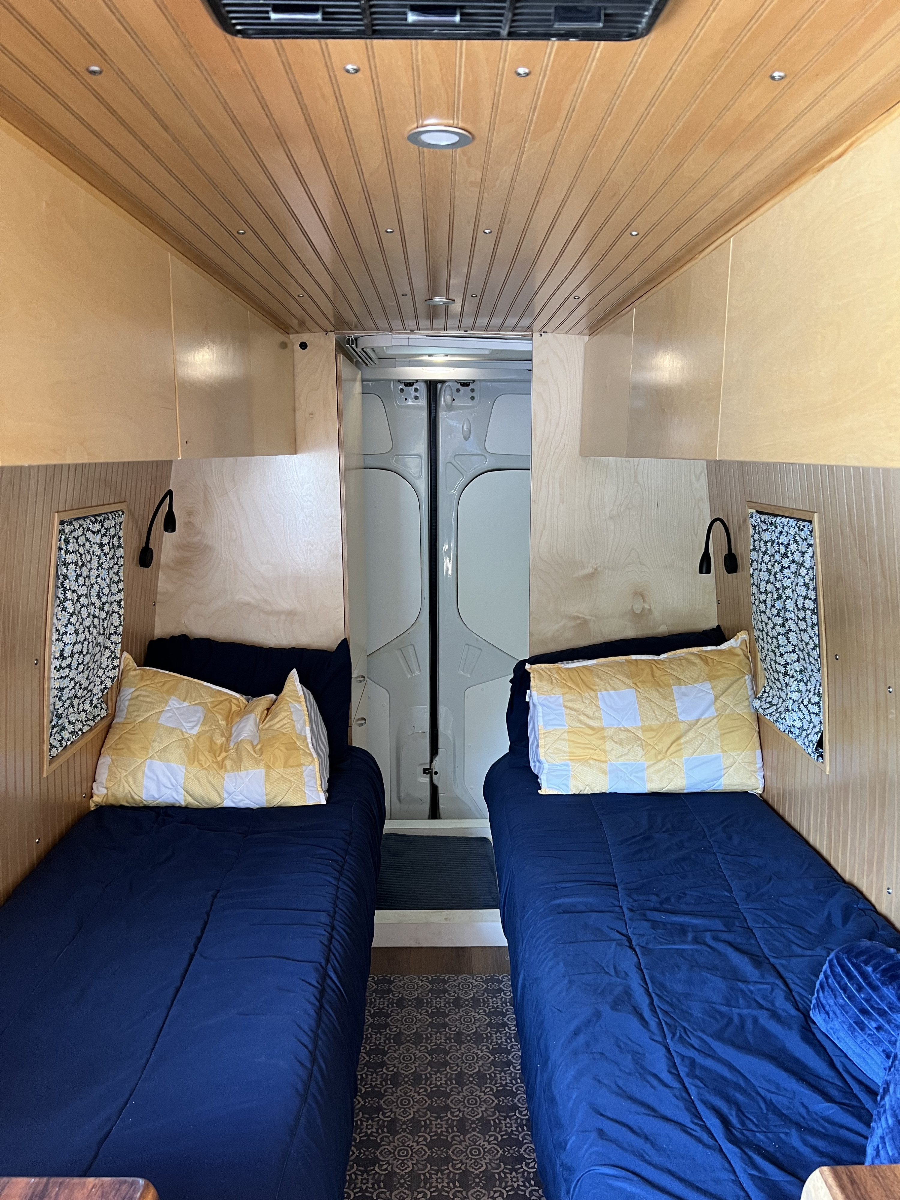 Cozy rv rental interior: two single beds with blue comforters, yellow pillows, wood paneling, and reading lamps.. Mercedes Benz Sprinter 2500 2019