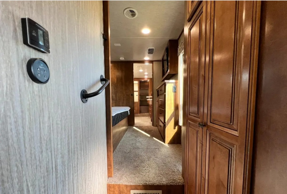 Step inside this RV rental's inviting interior: a hallway with modern controls, a bed, and rich wooden cabinets.. Heartland RVs Big Country 2017