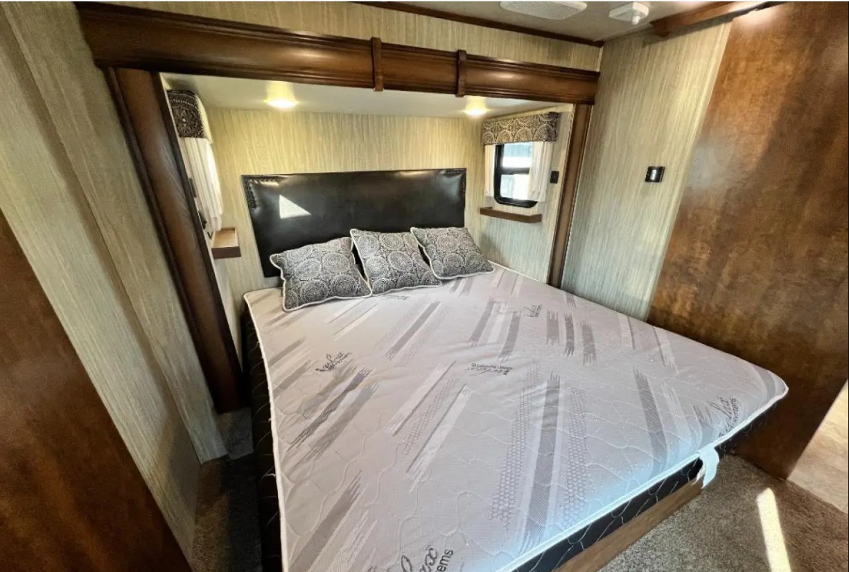 Spacious RV rental bedroom with a comfortable bed, dark headboard, and decorative pillows. Cozy and well-lit sleeping area.. Heartland RVs Big Country 2017