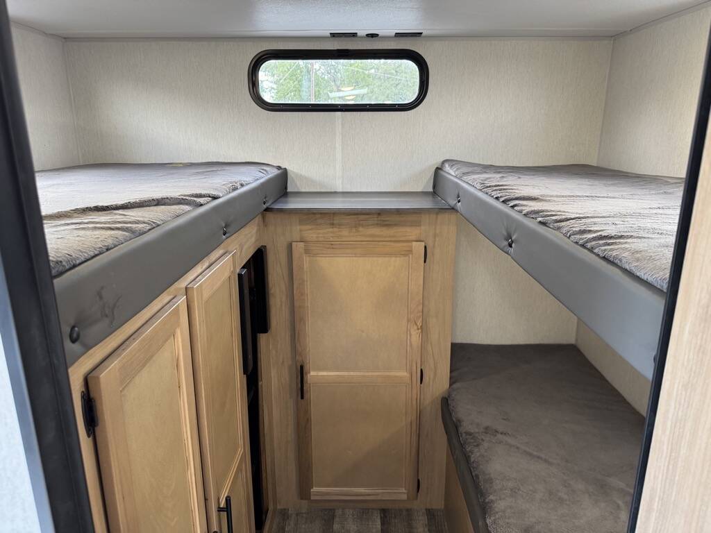 RV rental interior featuring comfortable bunk beds, practical storage cabinetry, and a small window.. Forest River Cherokee Grey Wolf 2023