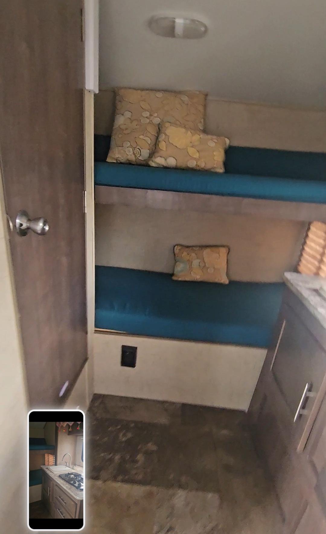 An RV rental interior reveals cozy bunk beds with teal cushions & patterned pillows, plus a compact kitchen counter.. Forest River 182 G 2016