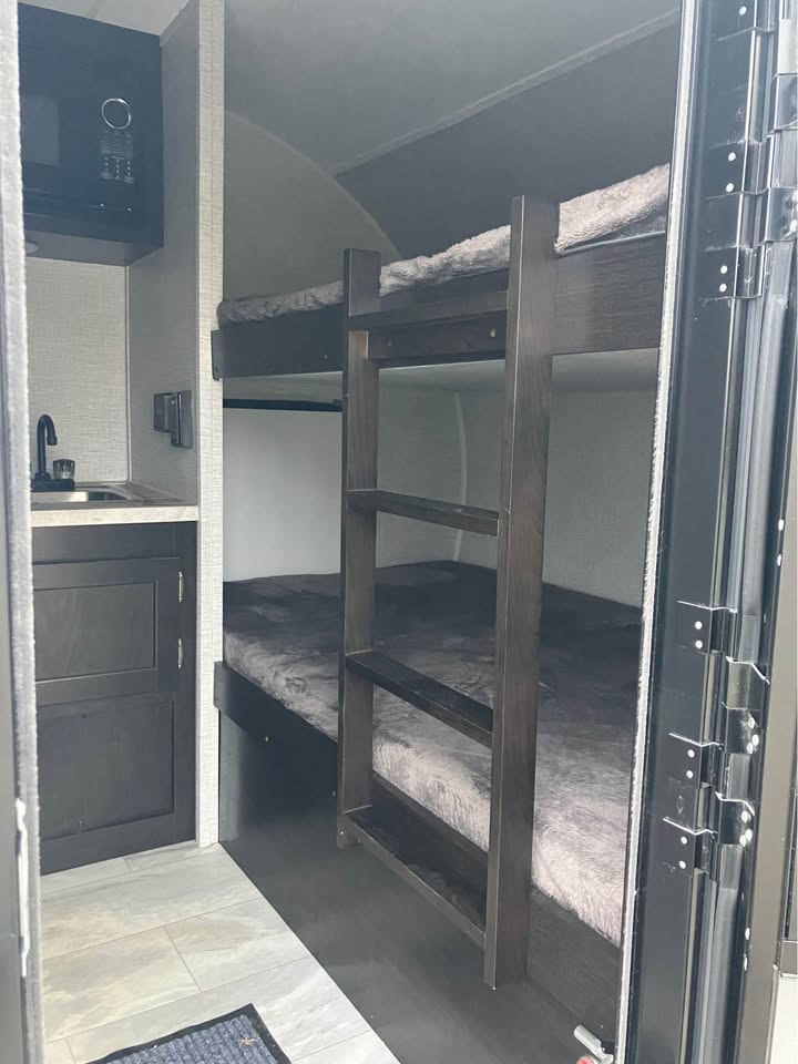 RV rental interior featuring cozy bunk beds and a compact kitchenette with a sink and microwave.. Braxton Creek Free Solo Plus 2022